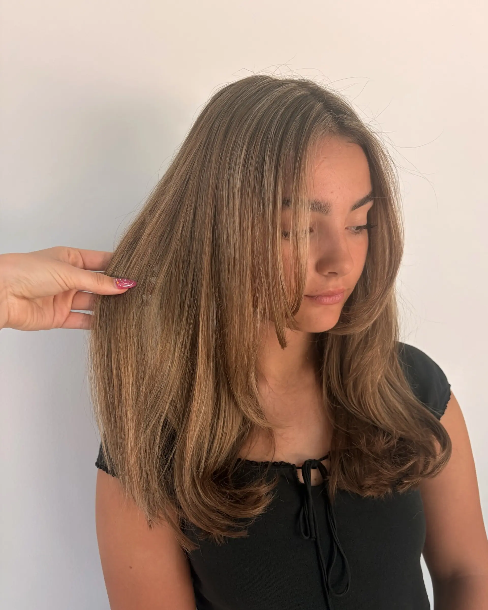 A long layered haircut styled in a smooth, voluminous blowout with gentle curved ends and face-framing layers, featuring soft sunkissed light brown and honey blonde highlights. 1