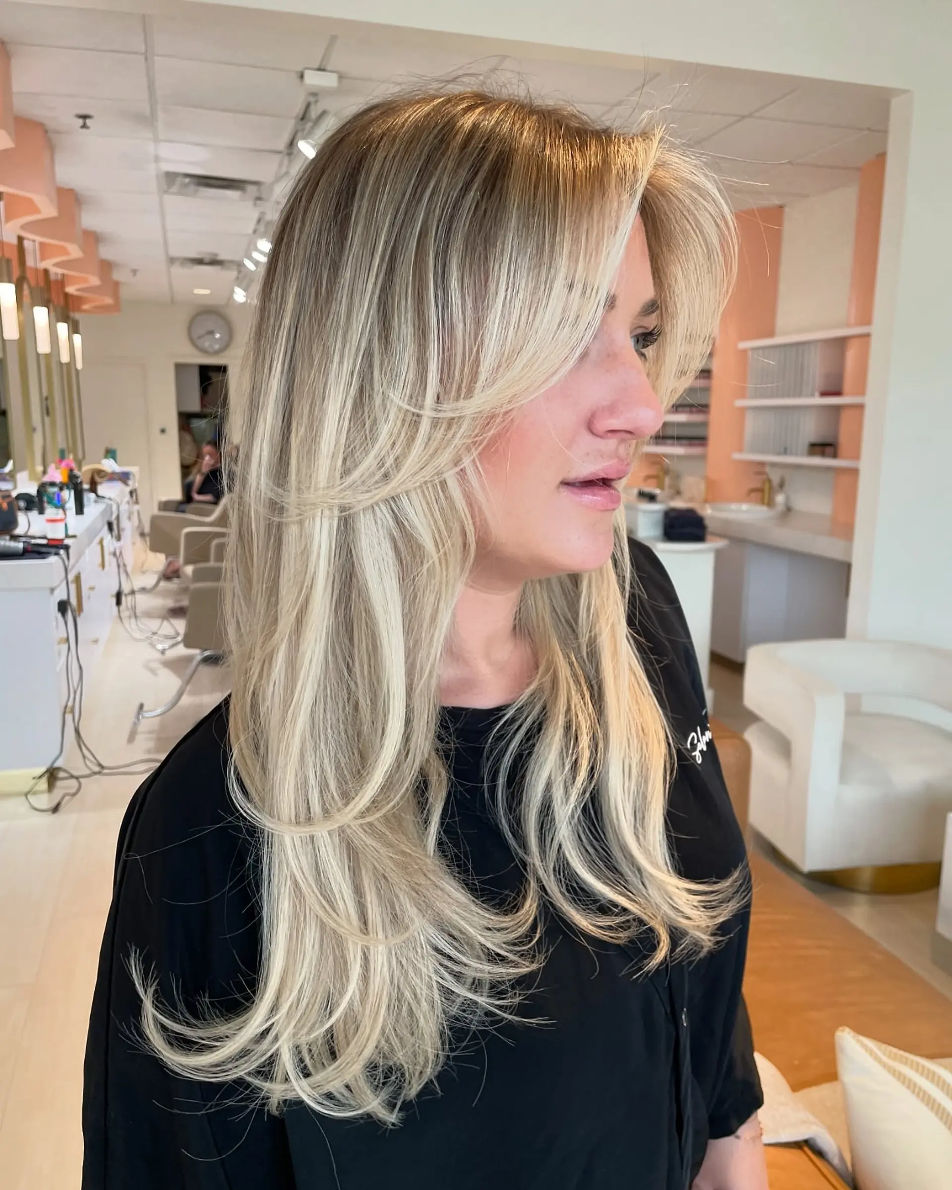 Long multi-tonal blonde hair featuring feathered face-framing layers and sweeping curtain bangs. 1