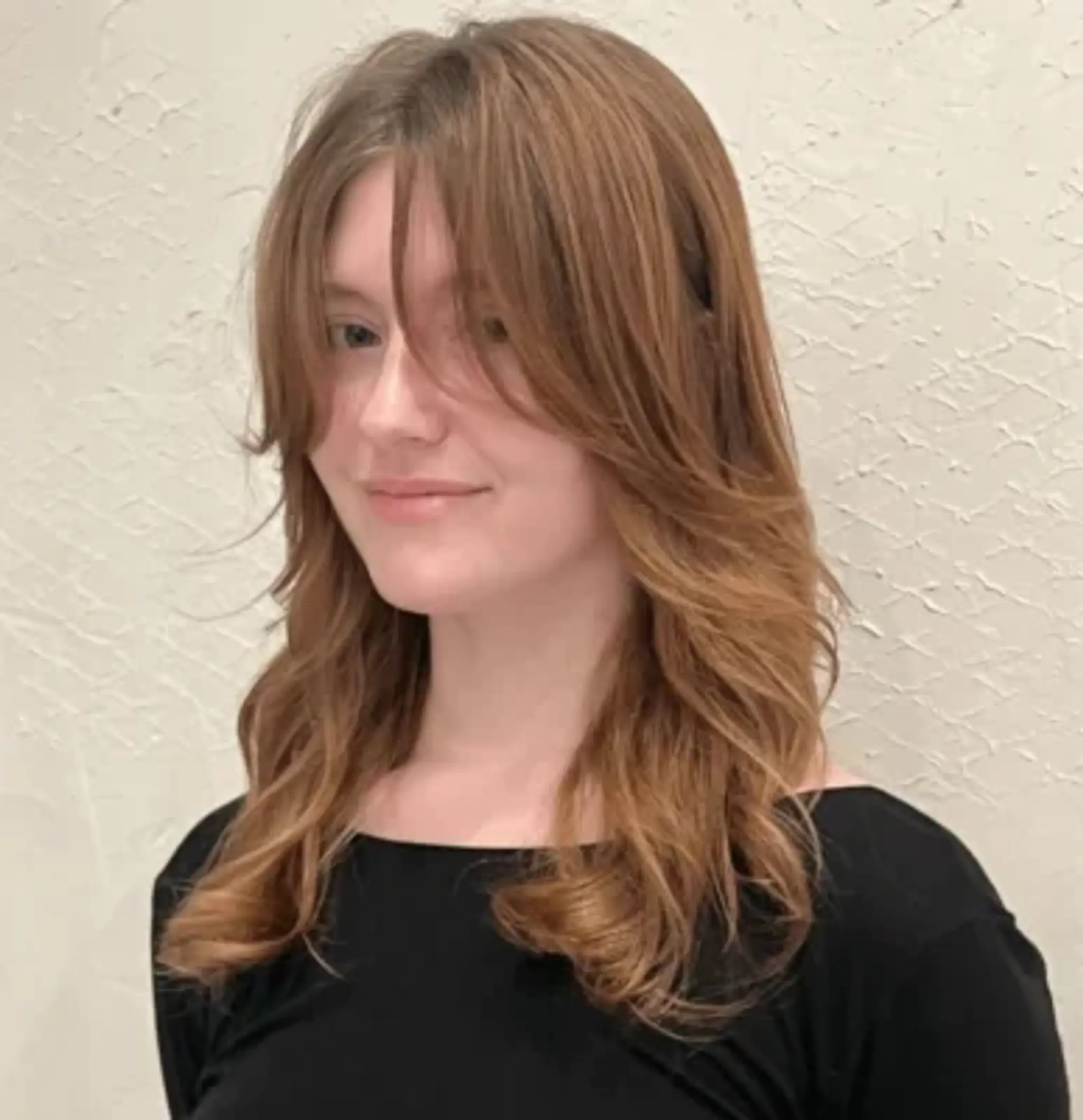 Medium-length, light brown hair with warm copper tones, layered with feathered bangs and natural waves.