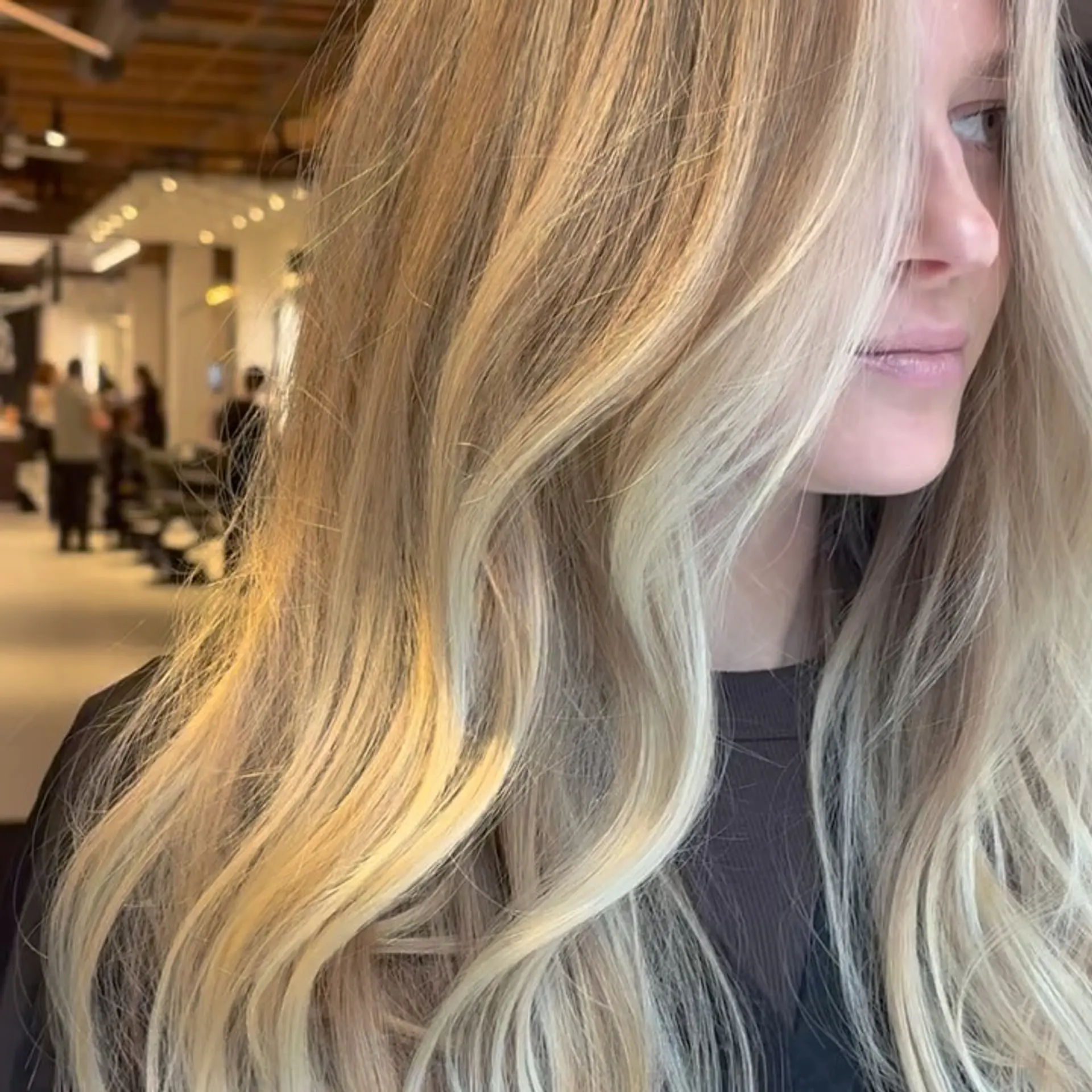 Long dimensional blonde hair styled into smooth, cascading soft waves with face-framing brightness. 1