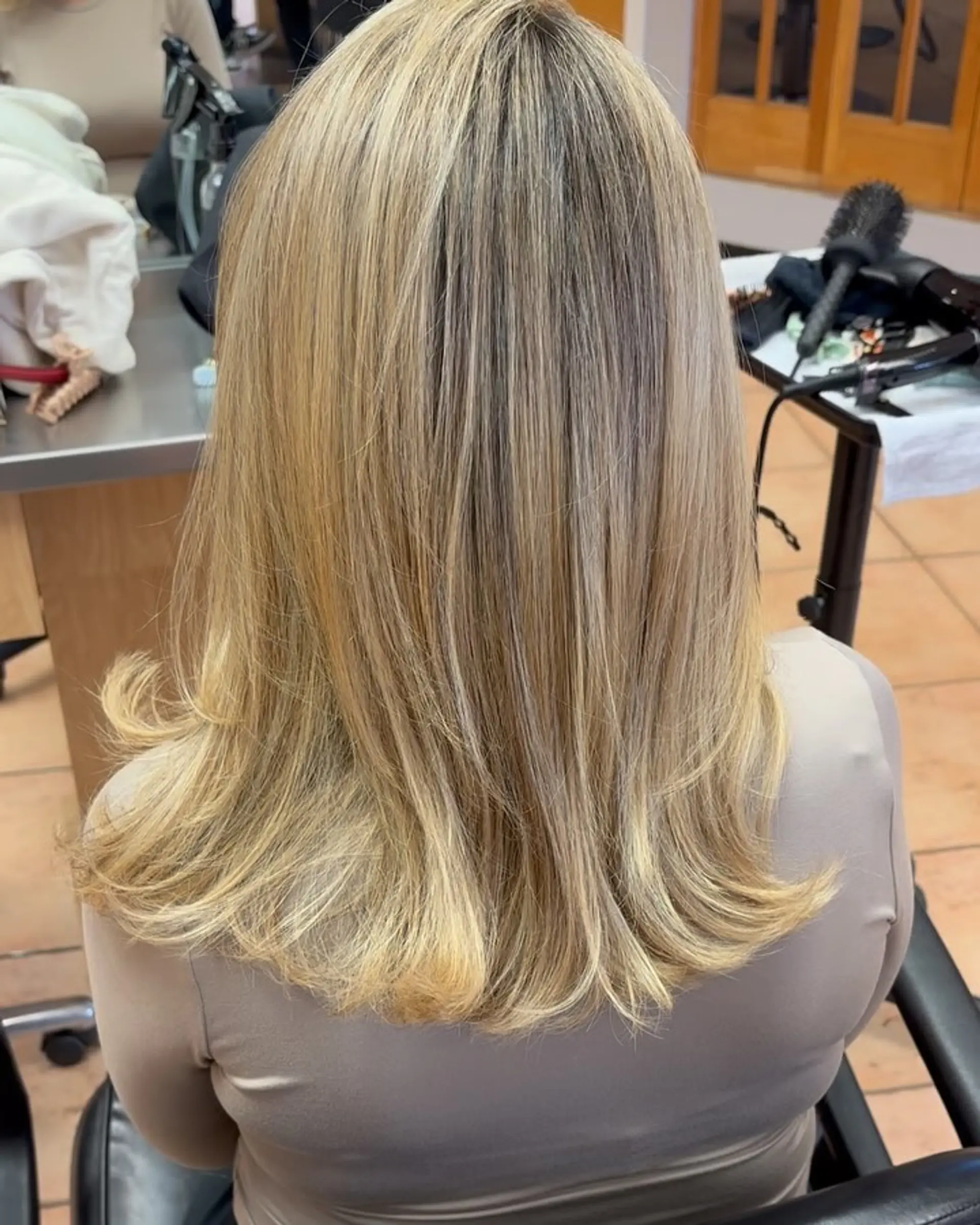 Medium-length layered blonde haircut styled smooth with flared, outward-flipped ends. 1