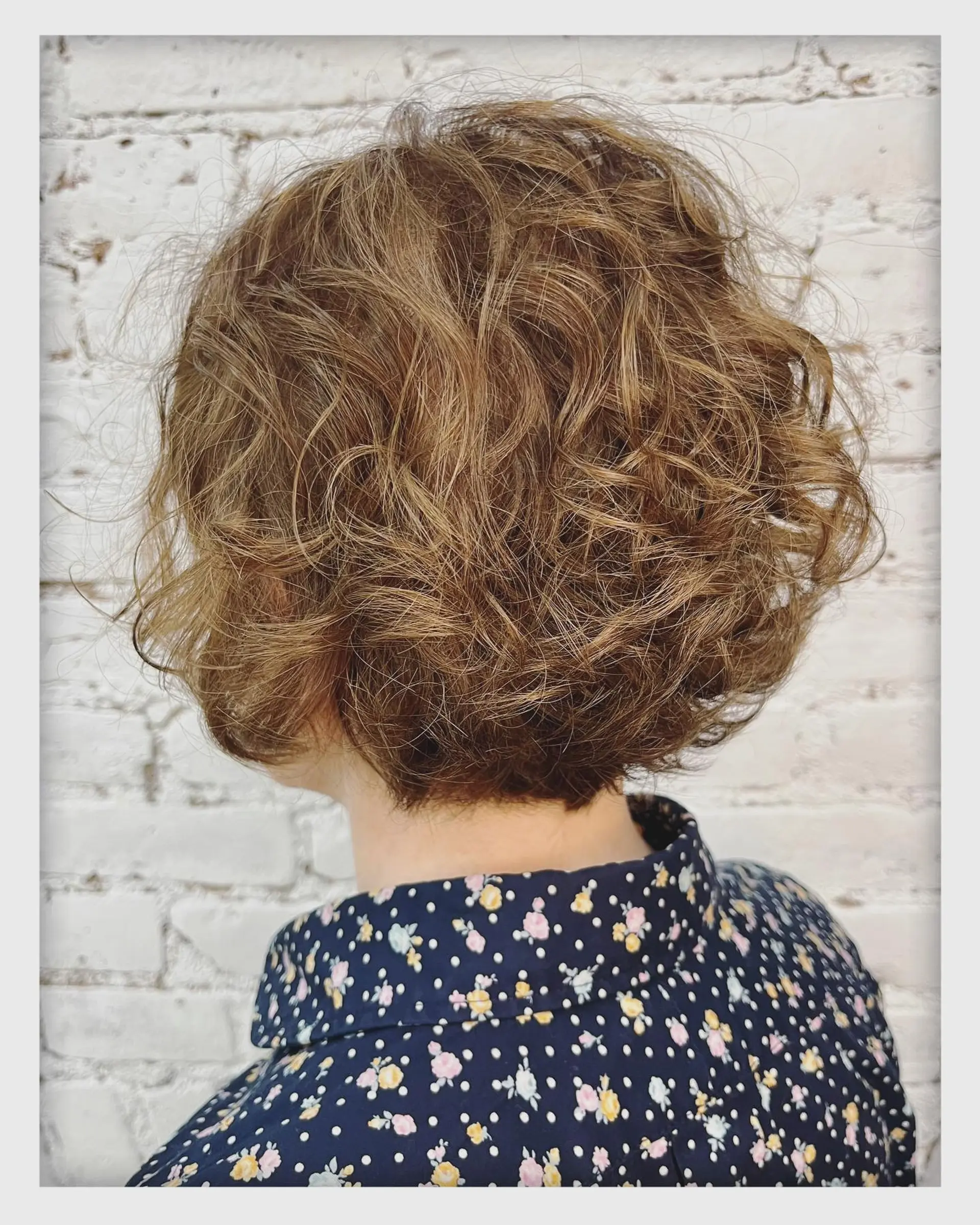 A voluminous, textured short curly bob shaped neatly above the nape. 1