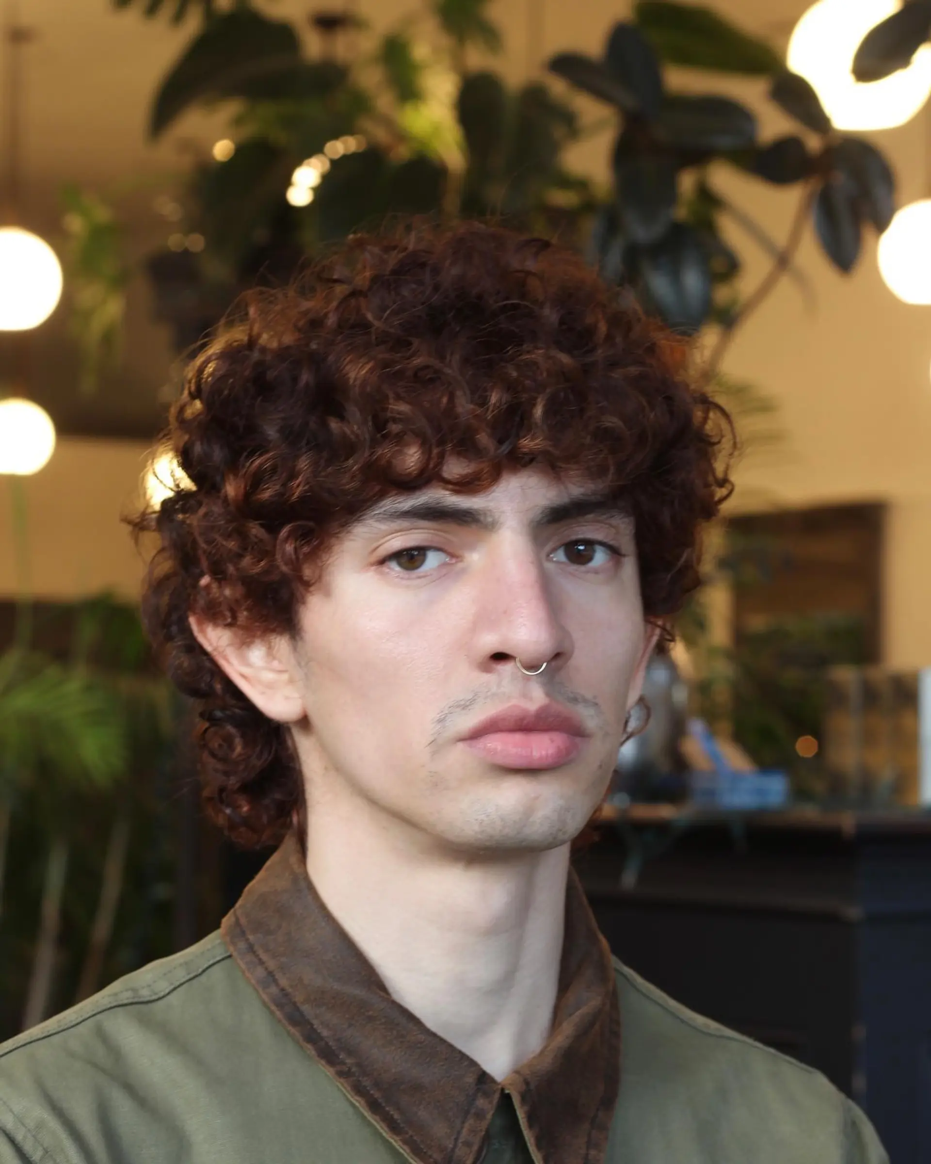 A layered, voluminous curly haircut with natural curl definition and forehead-skimming fringe in a rich auburn-brown tone. 1