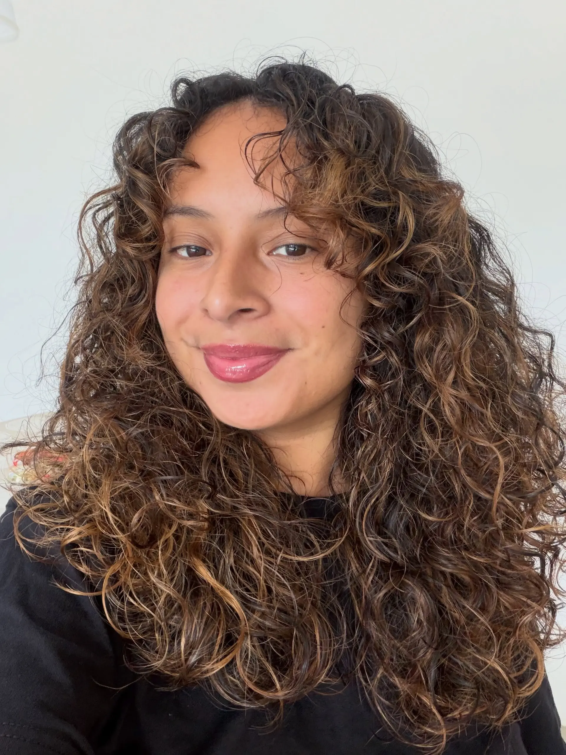 Voluminous long curly hair featuring a dimensional honey brown balayage with face-framing curl layers. 1