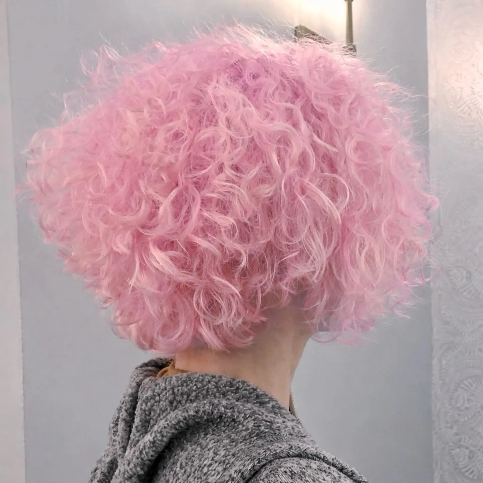A voluminous short curly bob dyed in an all-over pastel quartz pink shade. 1