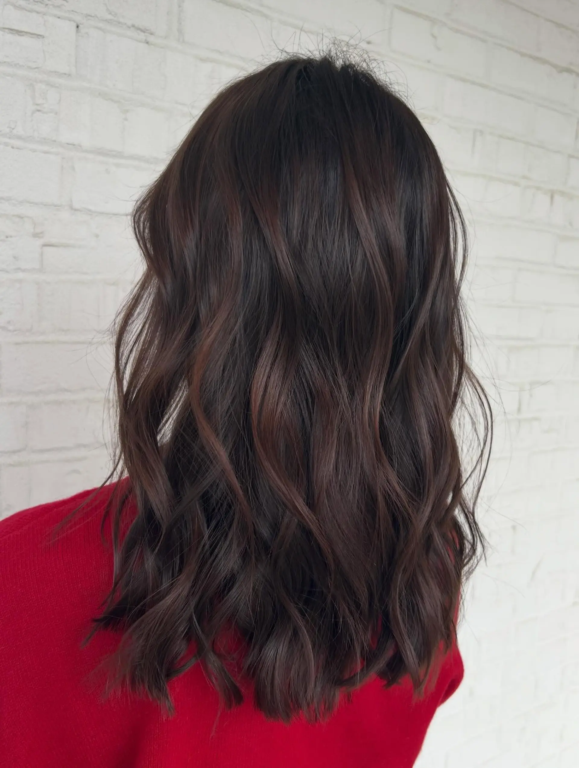 Medium-length dark brunette hair enhanced with rich cherry cola undertones, styled into soft, effortless waves. 1