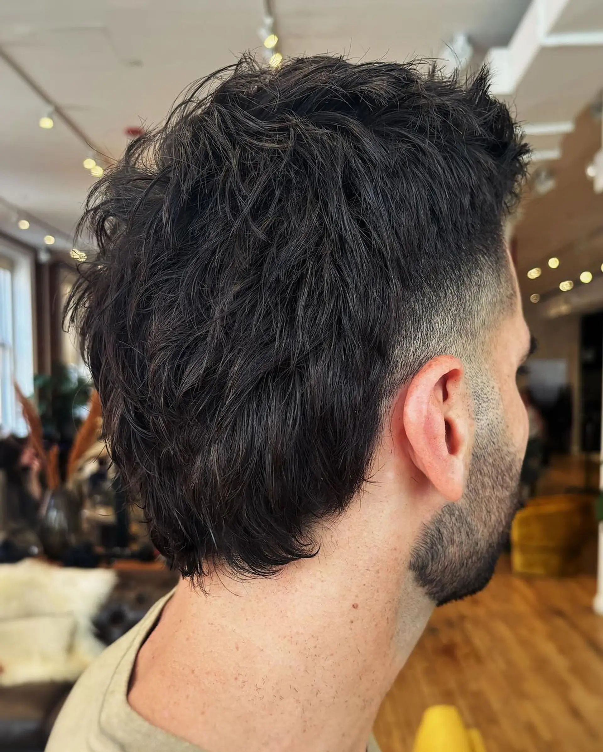 Short, Black, Wavy hair styled with a low fade on the sides and textured layers on top, creating a natural, tousled wave appearance with tapered sides for a classic silhouette. 1