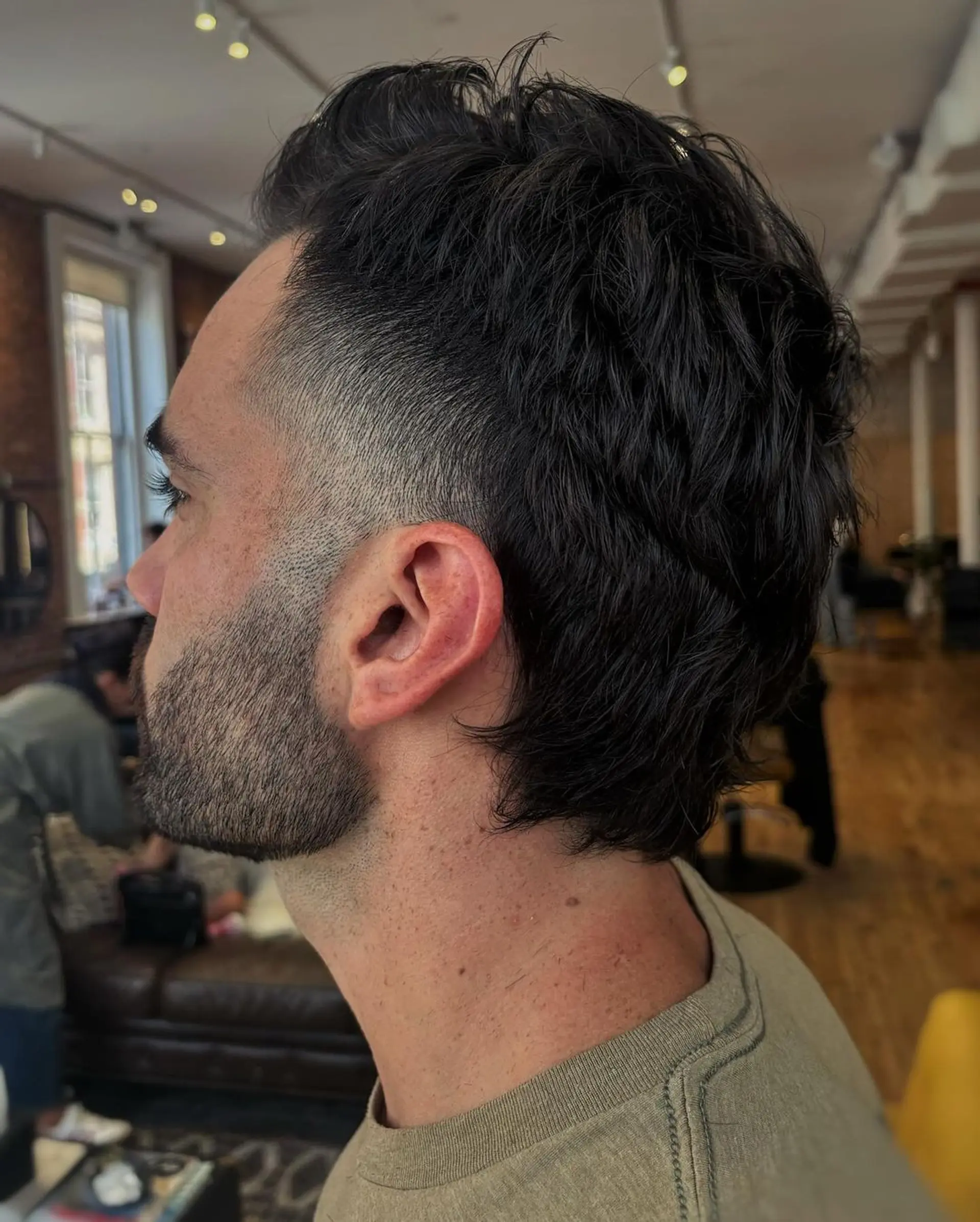 Short, Black, Wavy hair styled with a low fade on the sides and textured layers on top, creating a natural, tousled wave appearance with tapered sides for a classic silhouette. 2