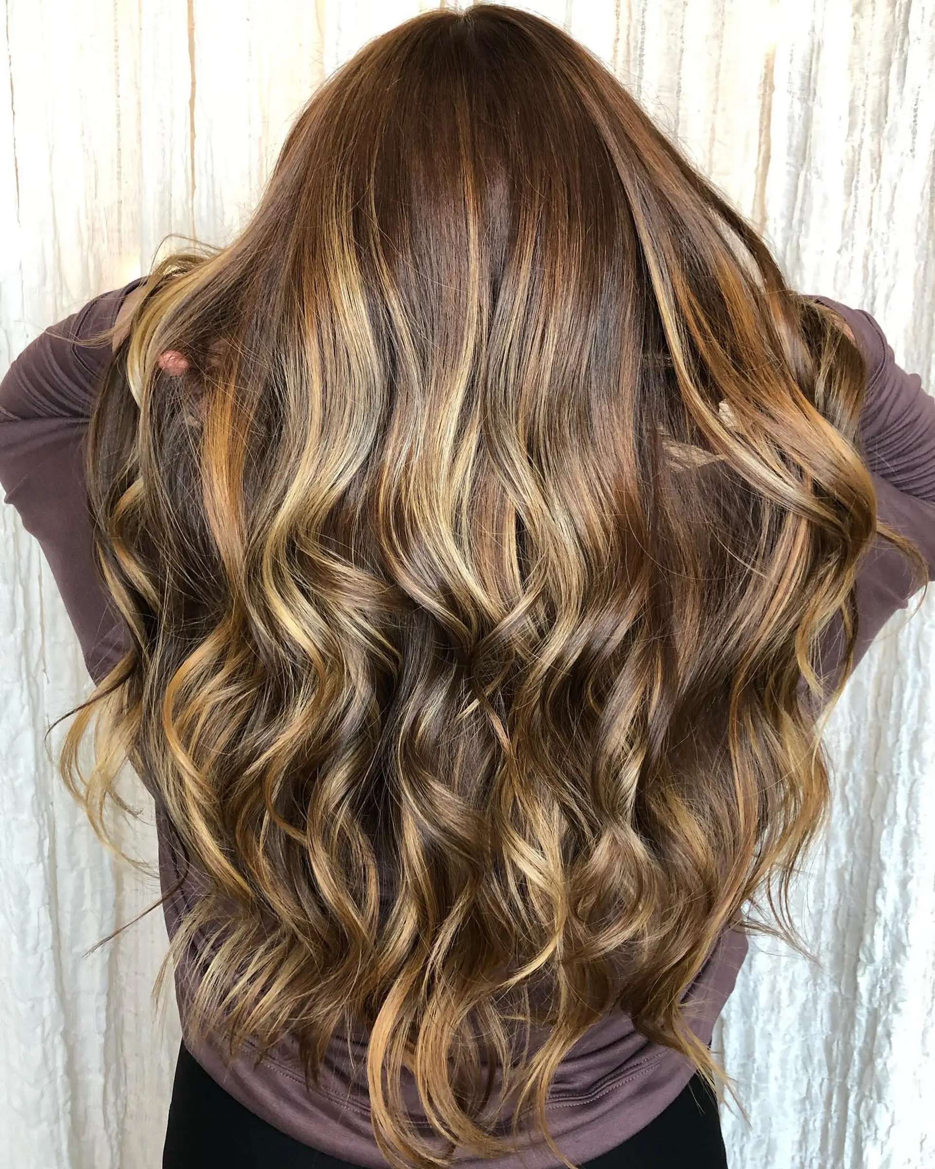 Long dimensional brunette hair styled in loose waves with blended warm caramel and honey blonde balayage highlights. 1
