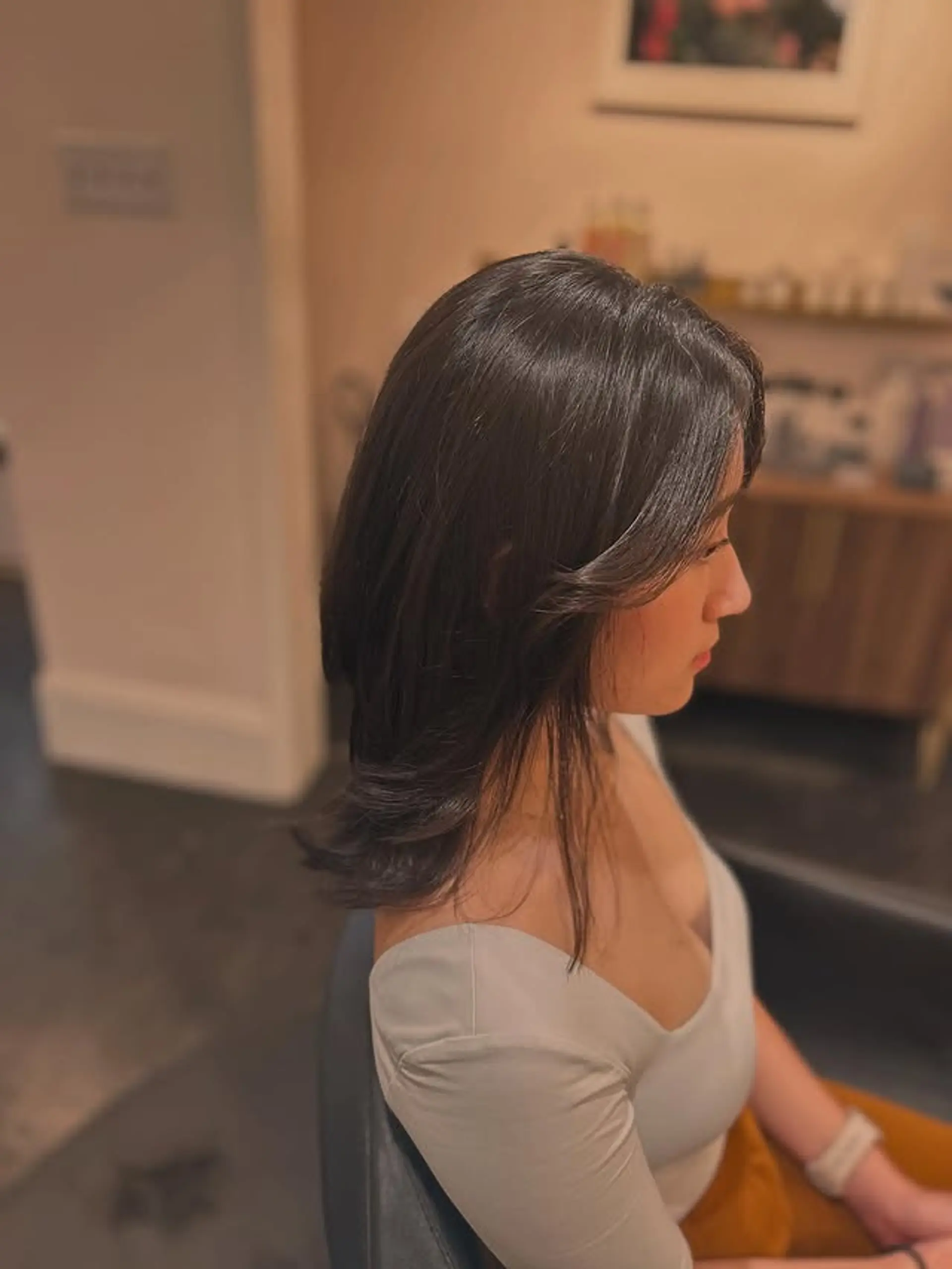 This haircut features medium-length hair with soft, face-framing layers around the front and subtle layering throughout the ends. The style is finished with a slight curl under, giving it a bouncy and polished look. 1