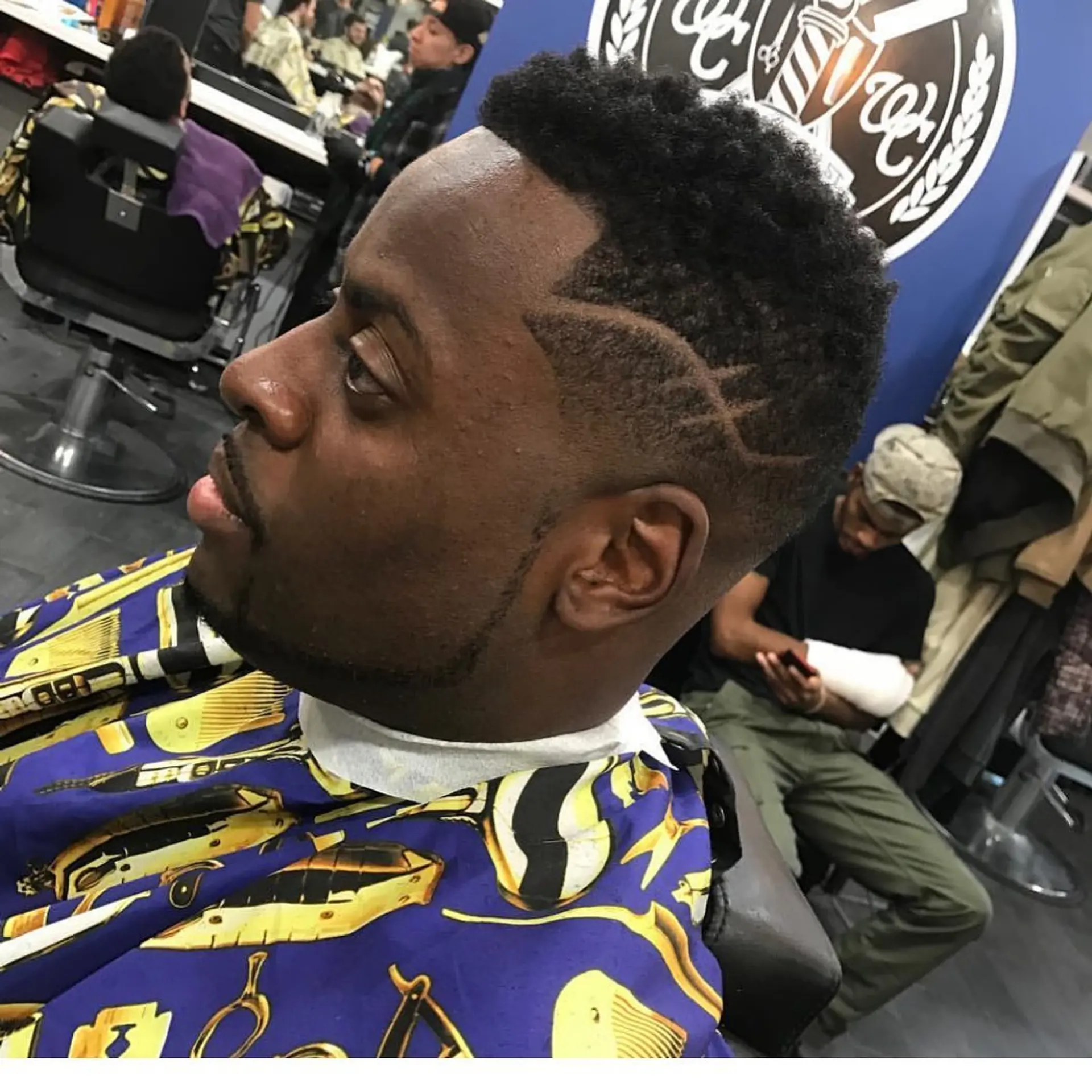 A sharp fade haircut featuring natural textured coils on top, a crisp line up, and custom shaved geometric line designs on the temple. 1