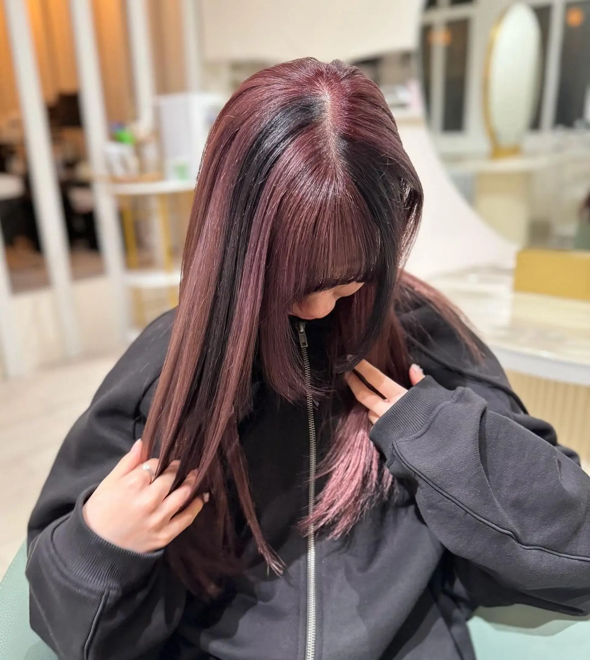 Long, straight burgundy hair with hints of black, featuring a prominent fringe and sophisticated ombre effect. Layers add movement and volume, enhancing the silky texture and polished finish. 1