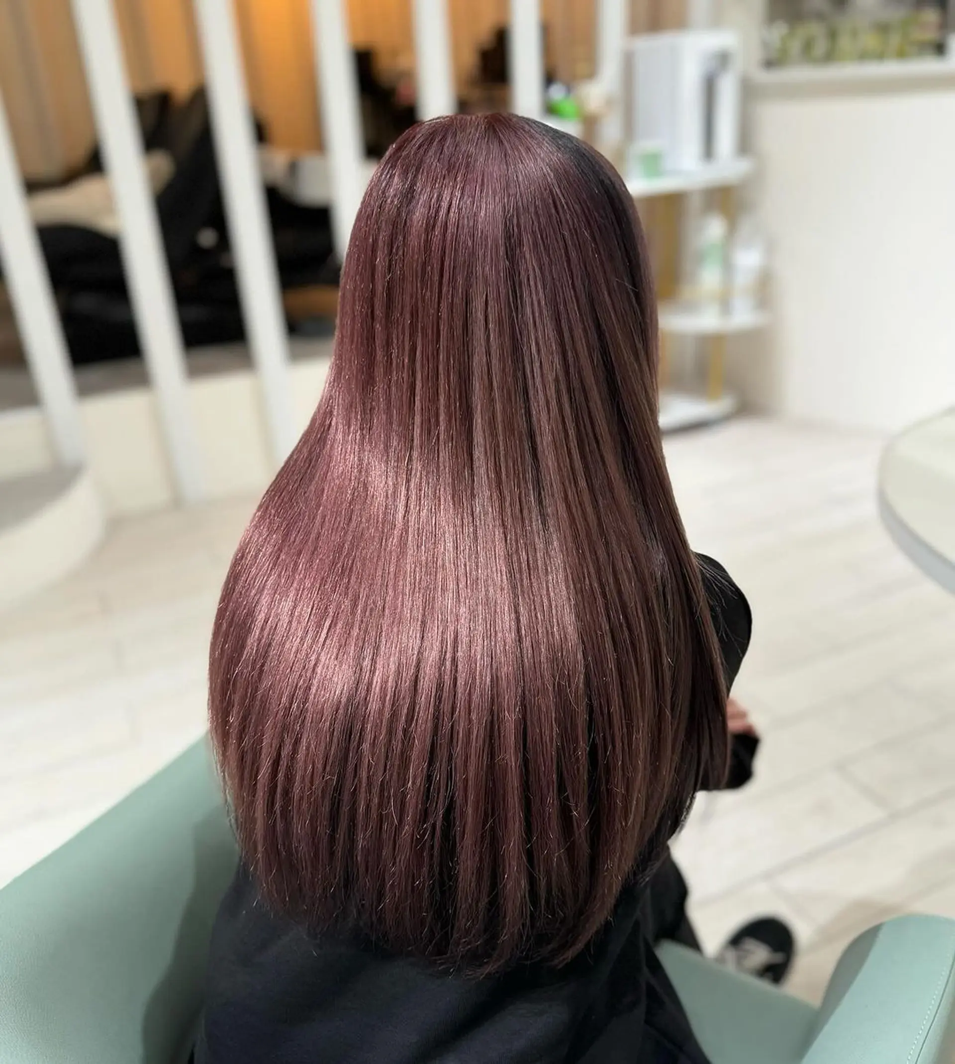 Long, straight burgundy hair with hints of black, featuring a prominent fringe and sophisticated ombre effect. Layers add movement and volume, enhancing the silky texture and polished finish. 2