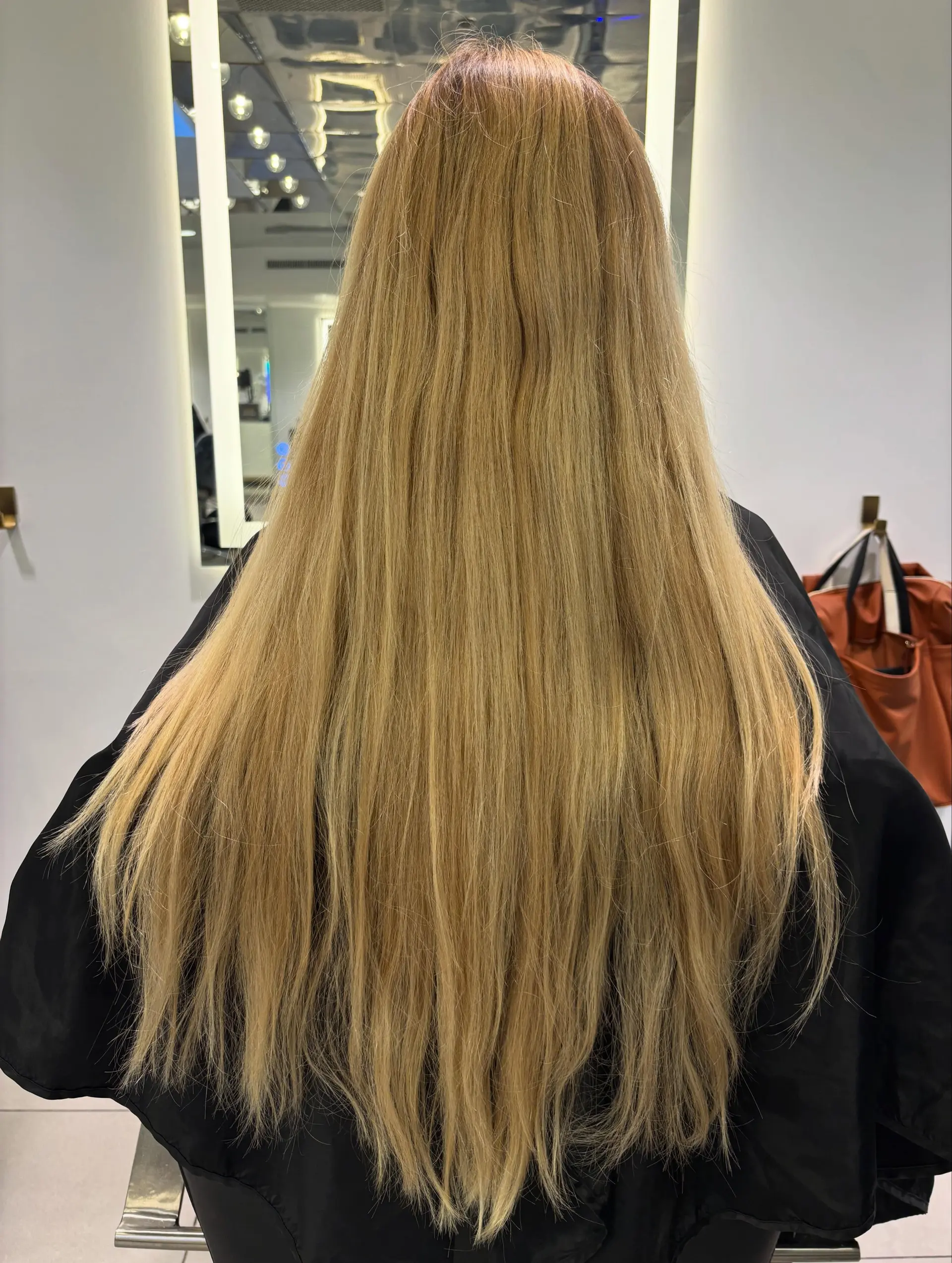 A sleek, long warm honey-blonde hairstyle worn straight down the back with soft textured ends. 1