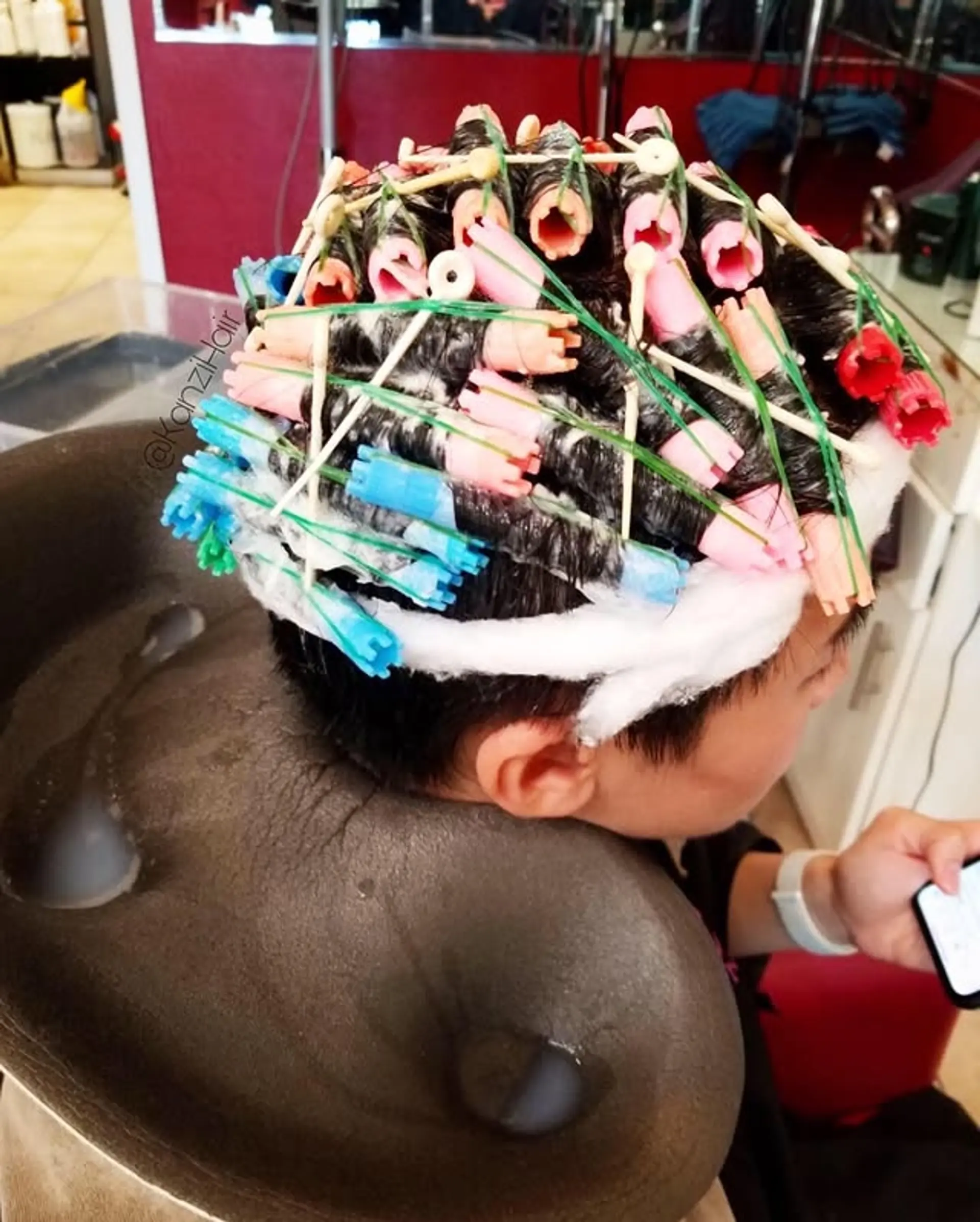 A permanent wave in progress, showing short hair wrapped in perm rods to achieve a curly, textured look. This service is designed to add lasting waves and volume, transforming straight hair into a dynamic, manageable curly style. 1