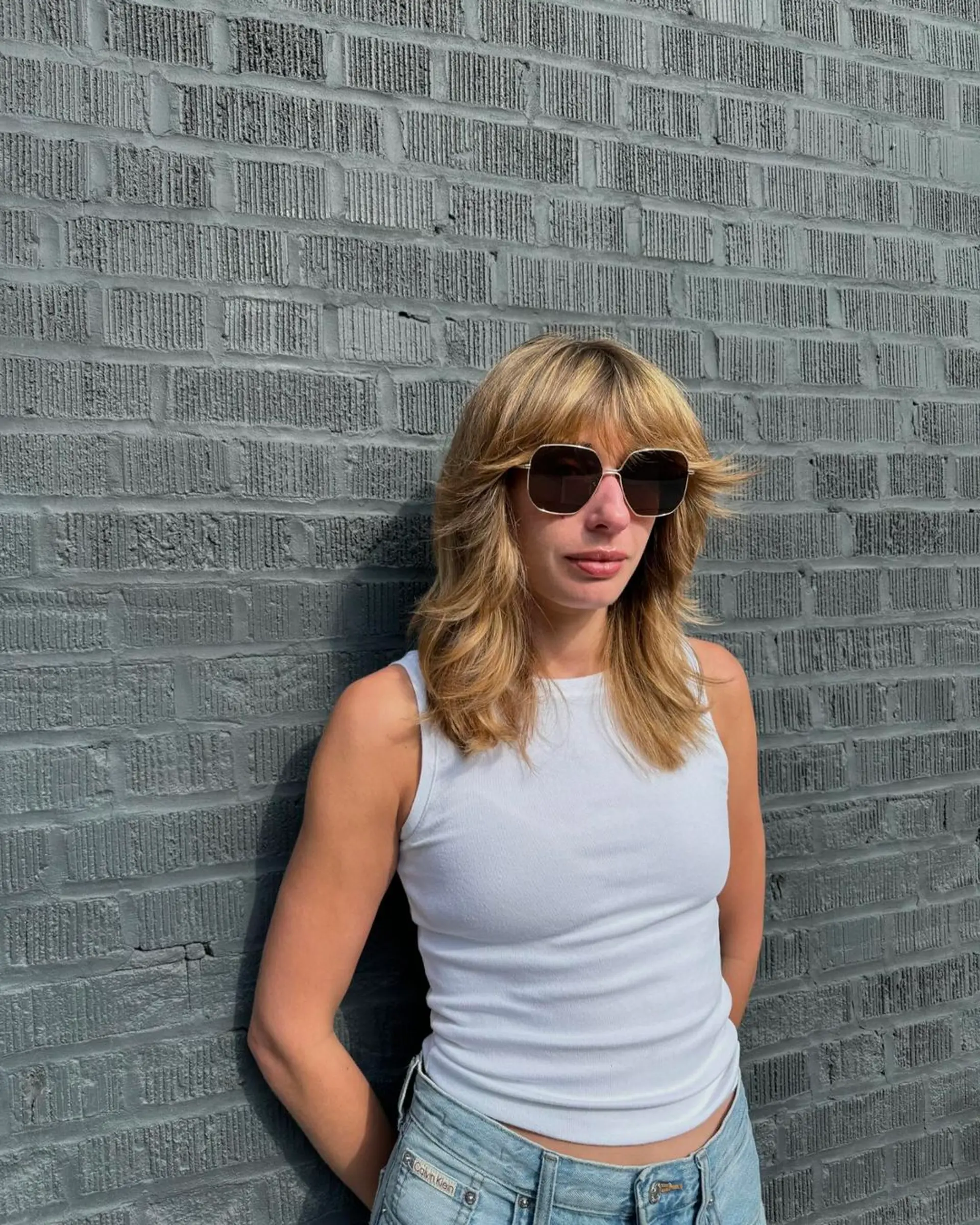 A medium-length, wavy blonde shag cut featuring face-framing layers and feathered bangs, accented with sun-kissed highlights. 1