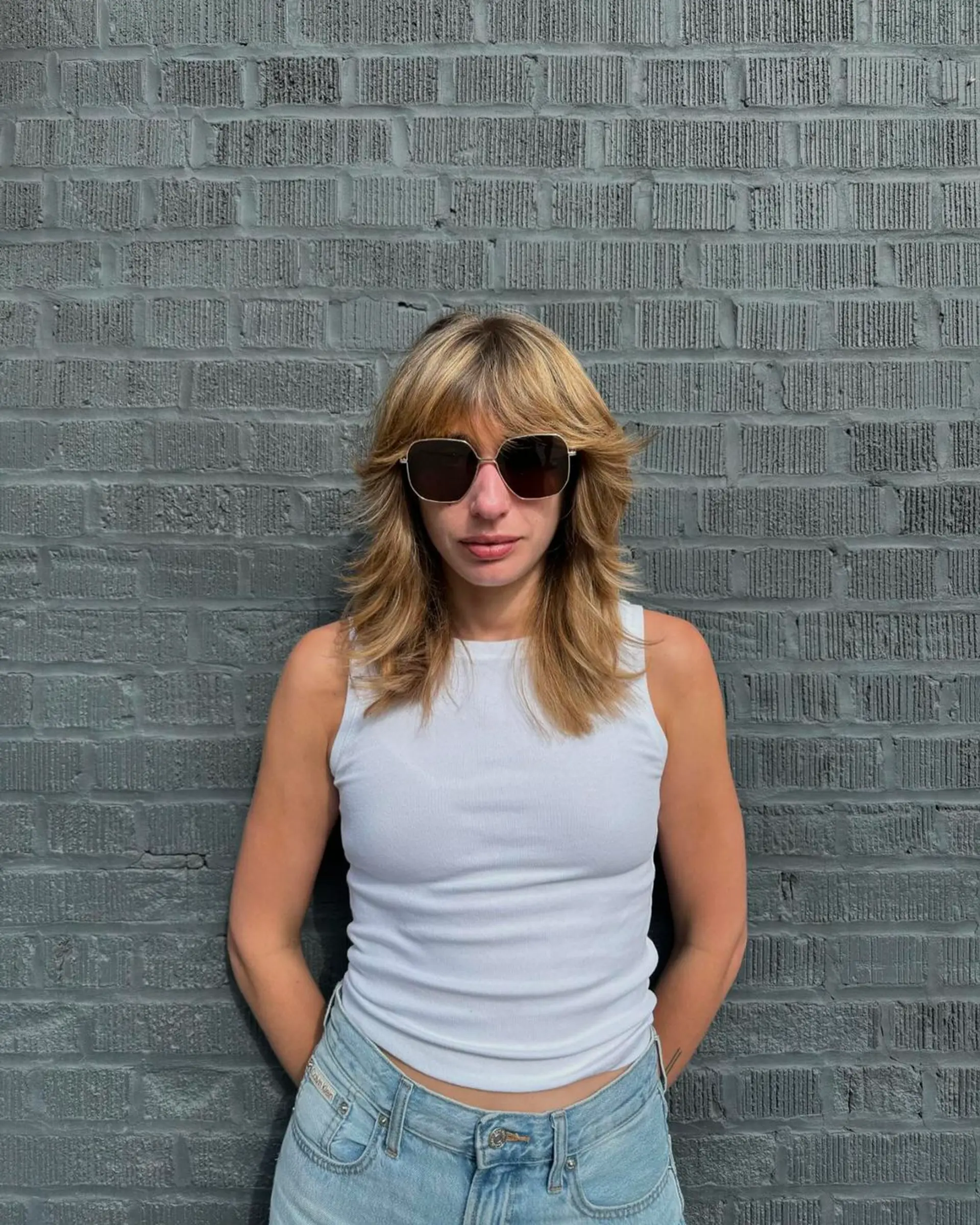 A medium-length, wavy blonde shag cut featuring face-framing layers and feathered bangs, accented with sun-kissed highlights. 2