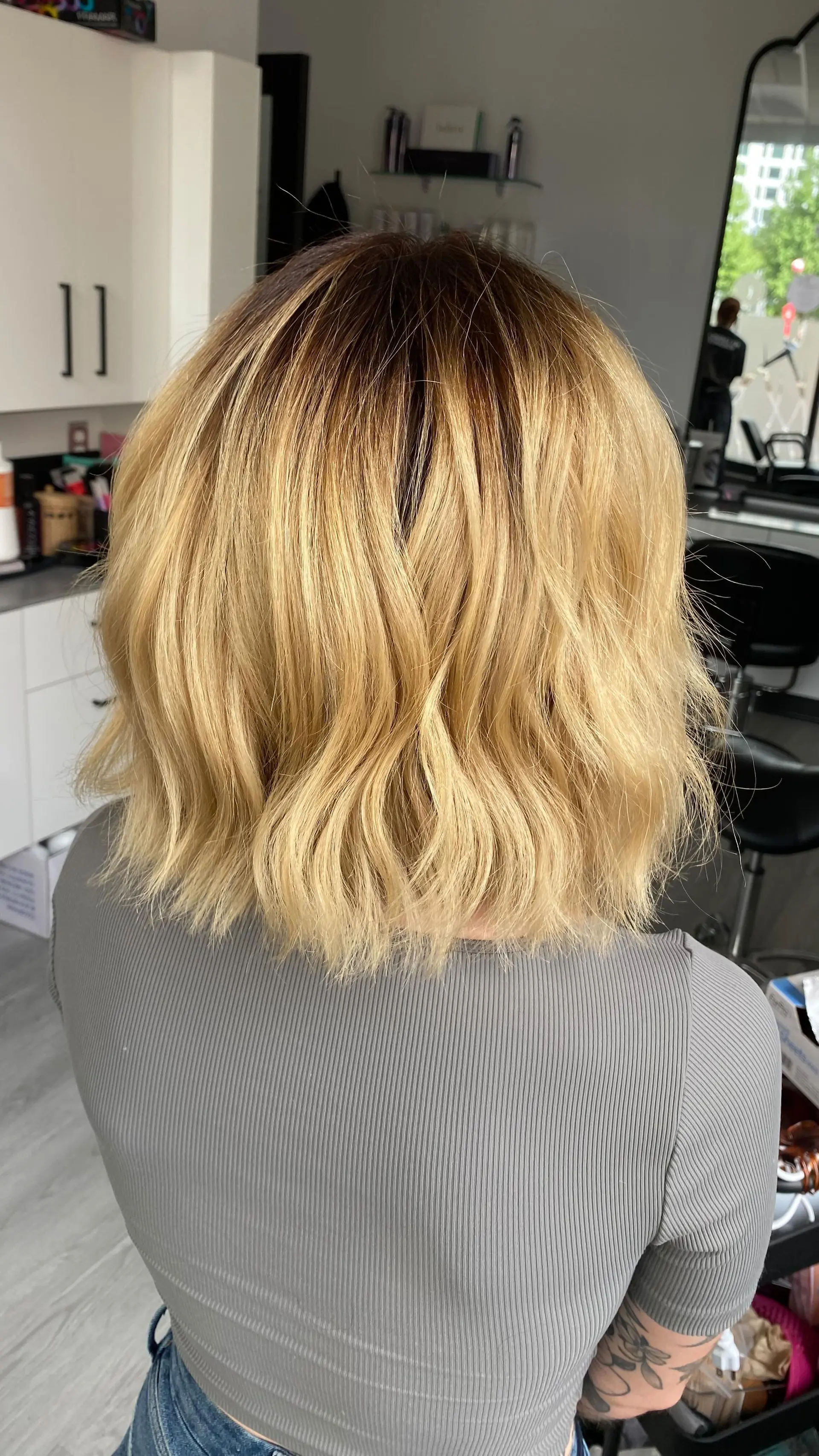 A textured shoulder-length bob styled in loose waves, featuring a dark brown shadow root blending into golden blonde tones. 1