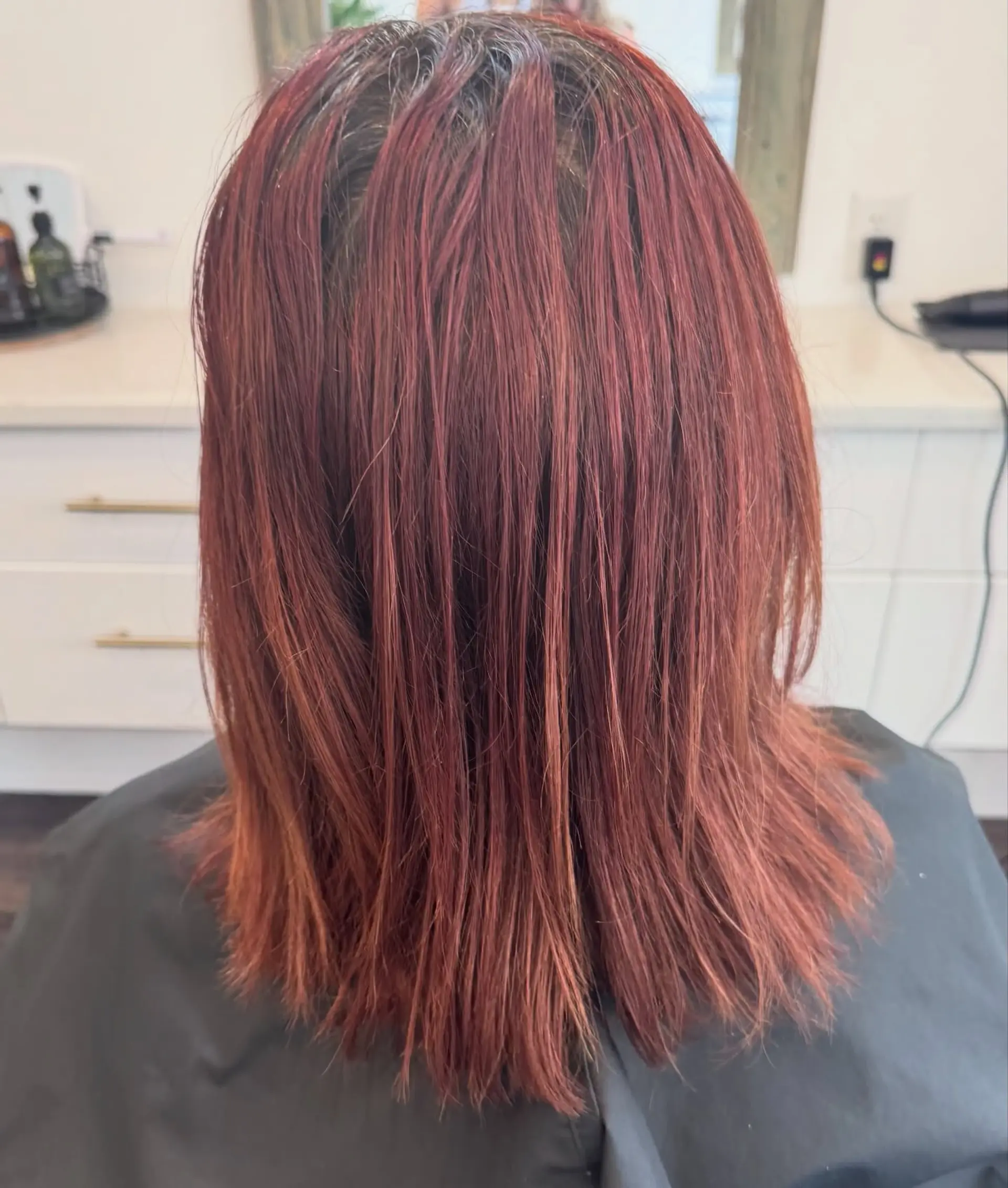 Medium-length straight hair styled down, showing warm auburn and muted red tones after a color correction process. 1