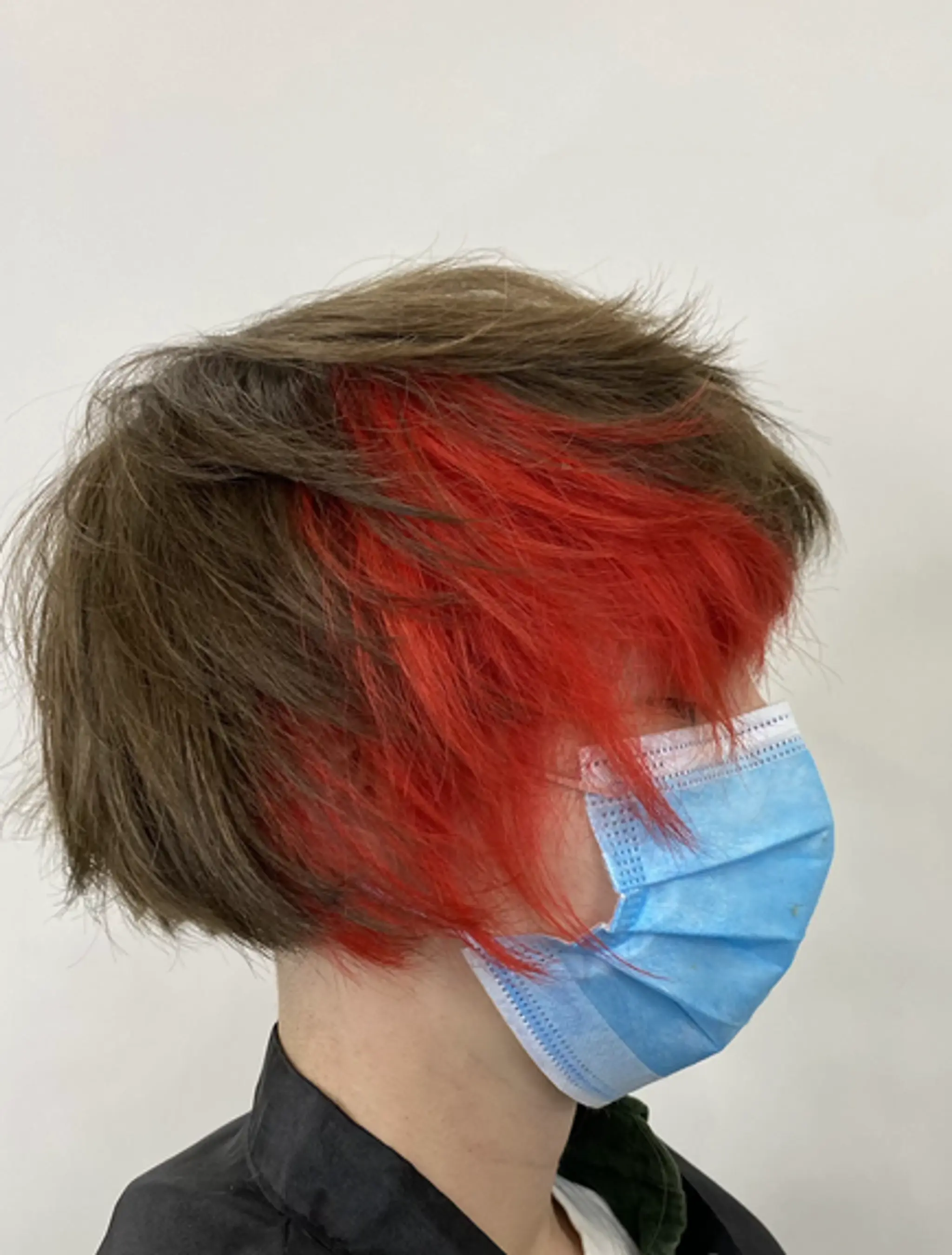 A short, layered bob with a natural brown base and a vibrant red underlayer, styled in a slightly messy fashion for a modern and edgy look.