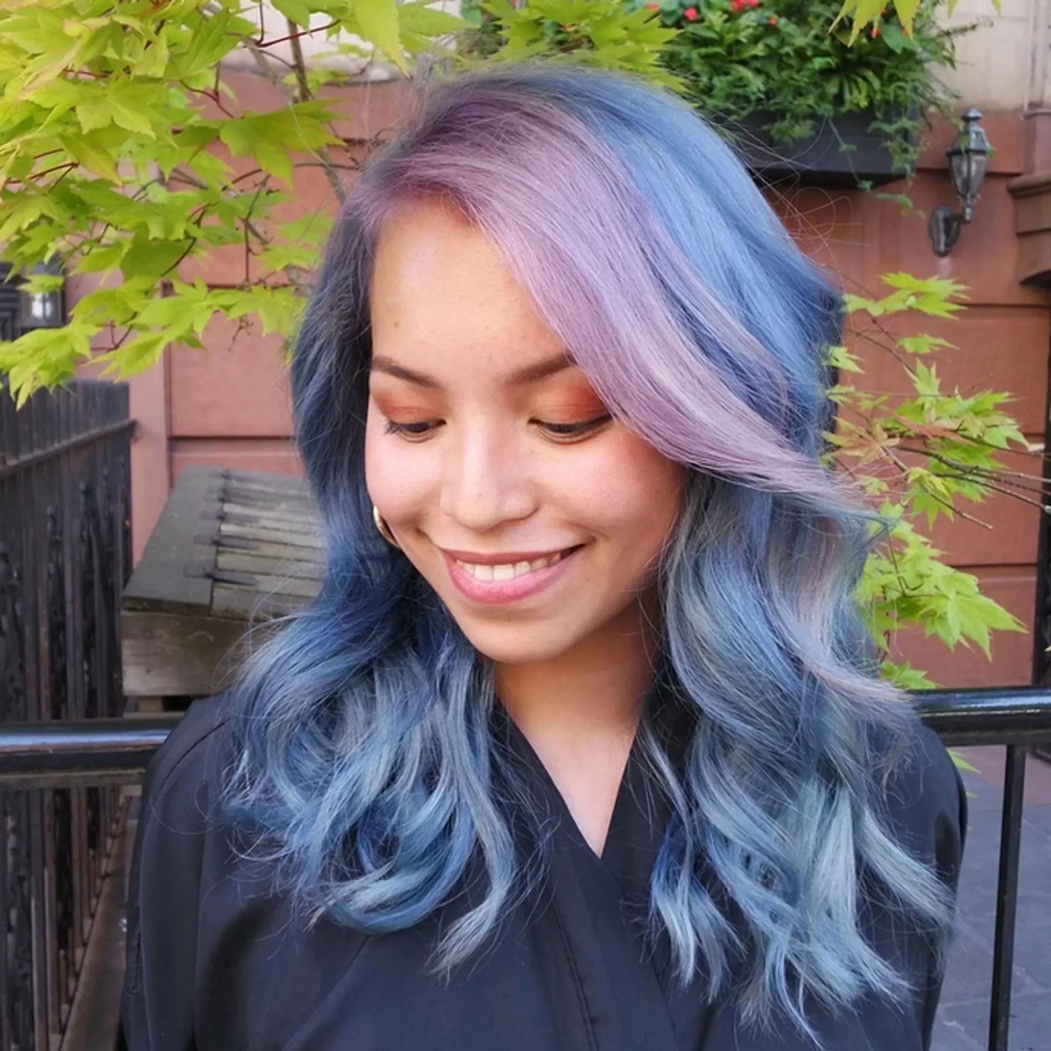 Medium-length wavy hair in iridescent pastel colors, transitioning from lavender to blue and light blue. Soft waves and a side part create a whimsical and ethereal look.
