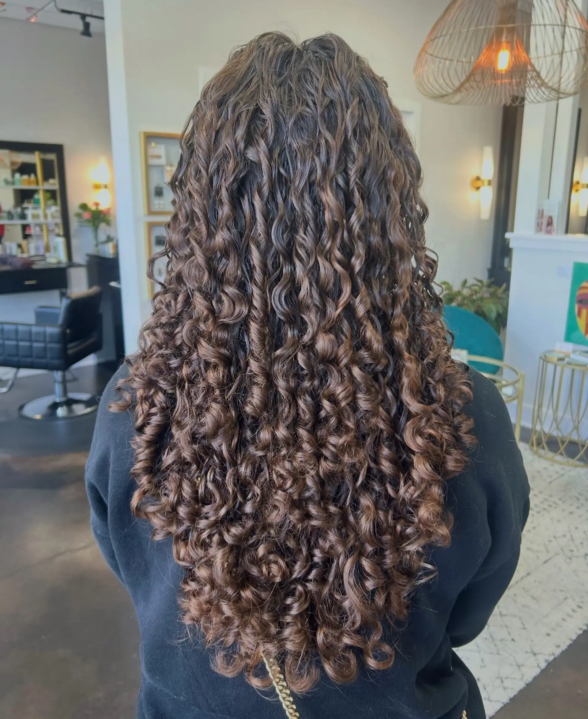 Long defined curly hair cut in a cascading shape with subtle chocolate and caramel balayage tones. 1