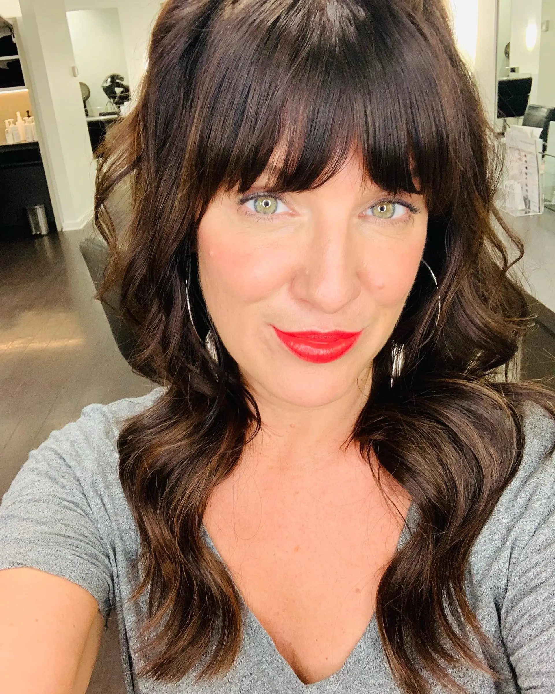 Long dark brown hair styled in soft, voluminous waves paired with a full textured fringe. 1