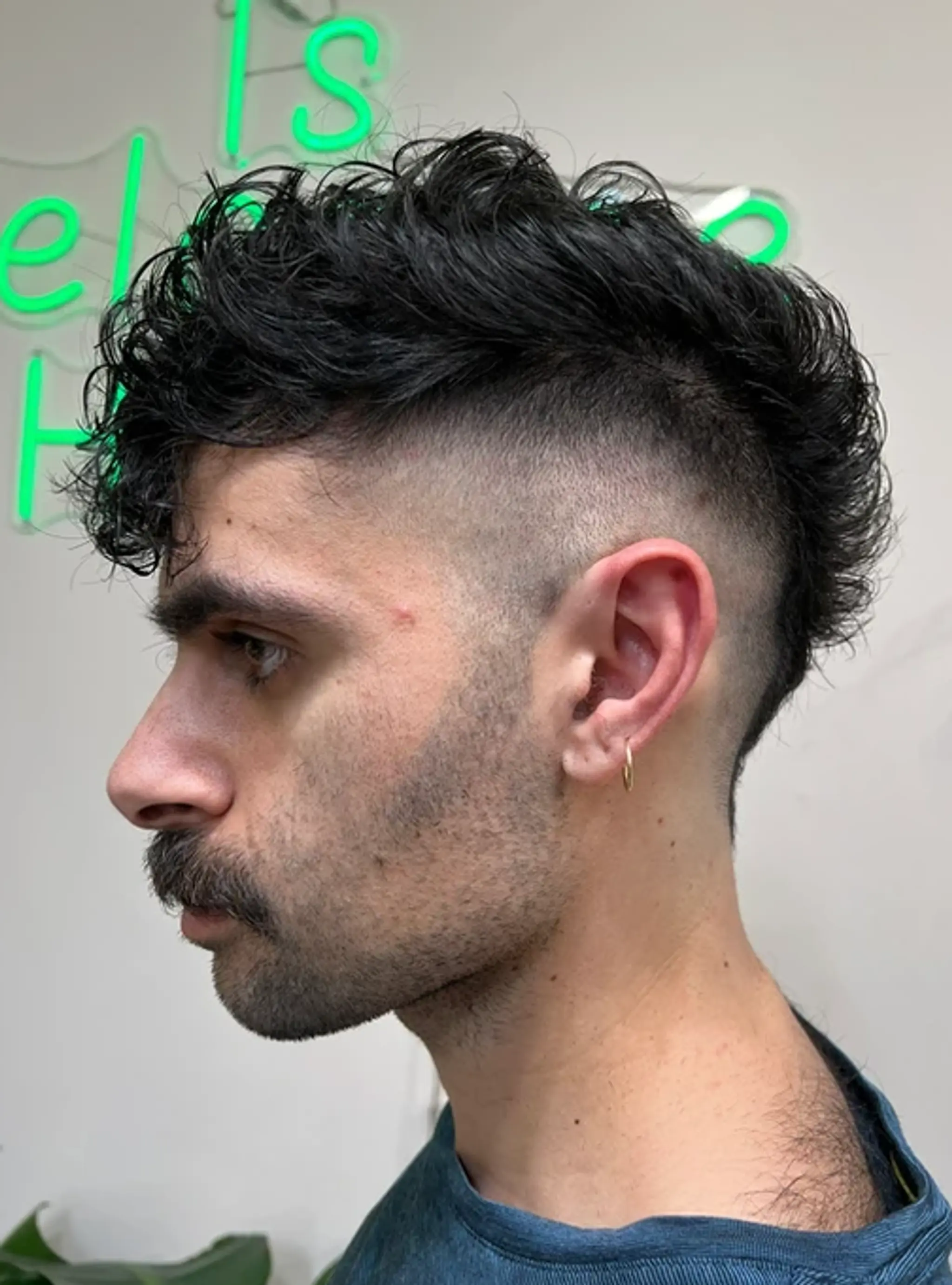 A curly undercut fade with black hair, featuring closely shaved tapered sides and a thick, curly top with a distinctive fringe.