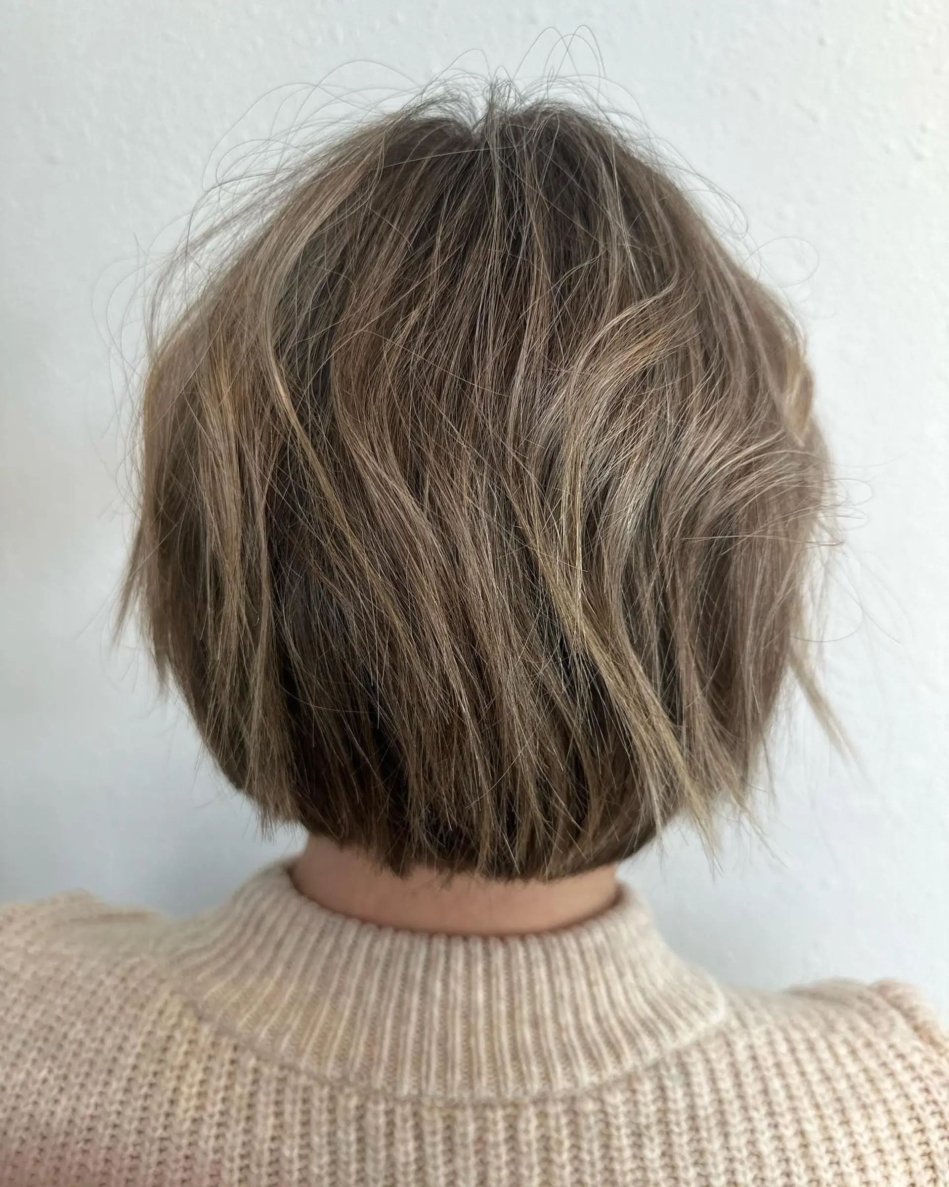 A textured short graduated bob haircut featuring subtle layers and fine ash blonde partial highlights woven throughout a light brown base. 1
