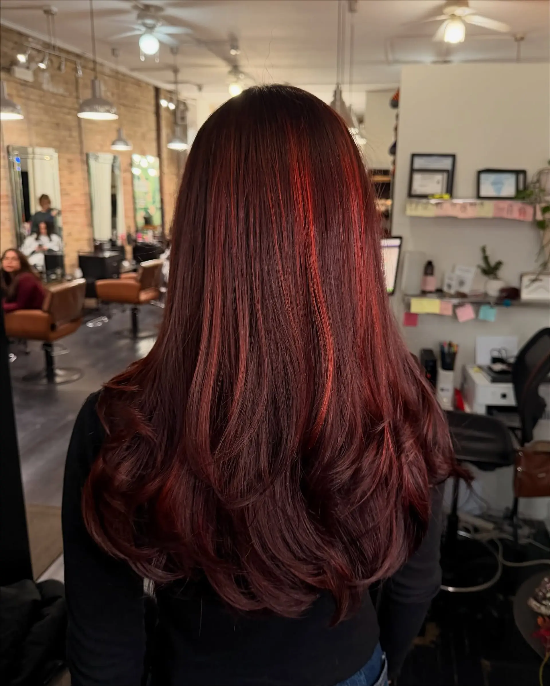 Long layered burgundy hair with vibrant red highlights, blow-dried sleek with curved, bouncy ends. 1
