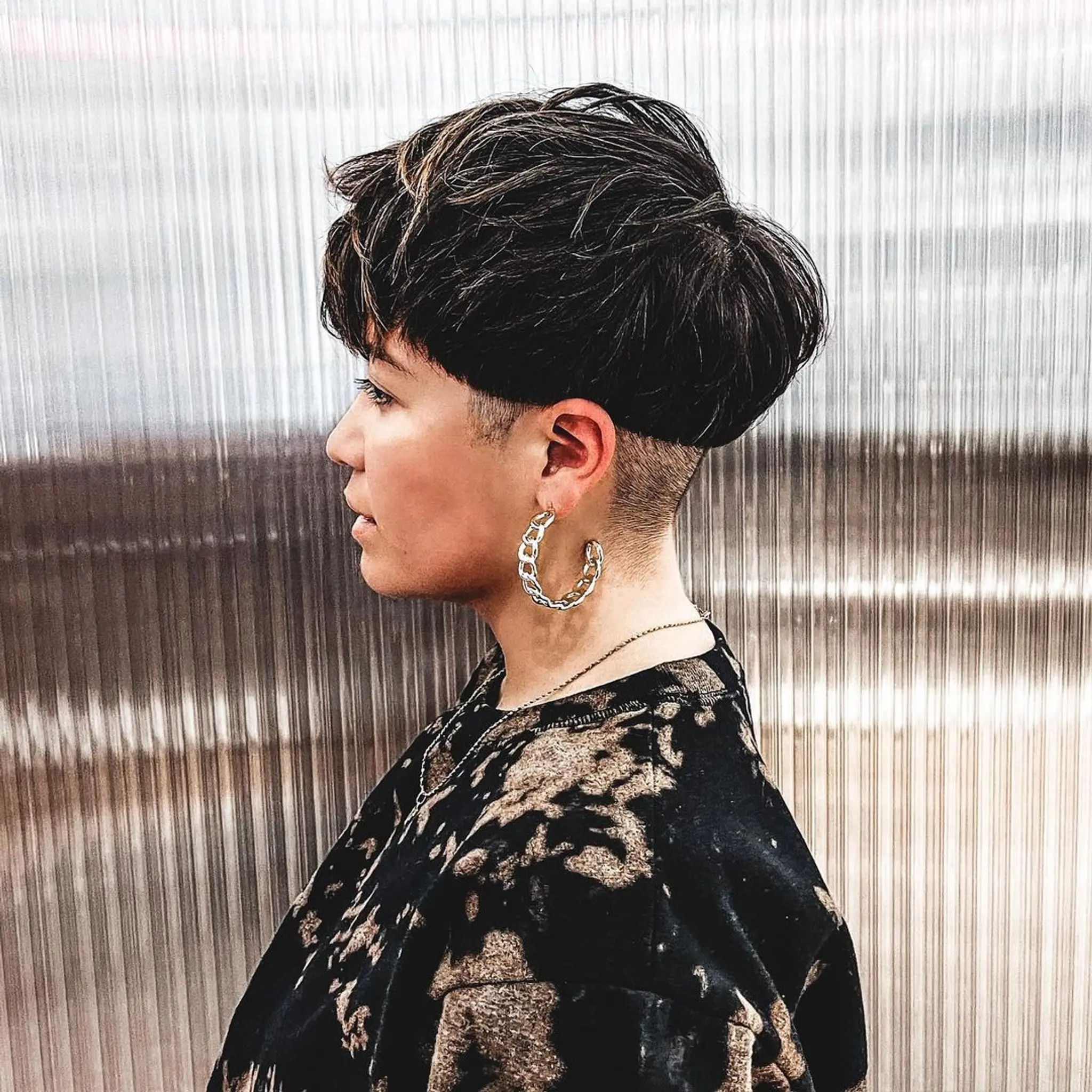 A sharp undercut with a gradual fade and highlighted tips. The top has volume and a slight pompadour effect, swept to the side.