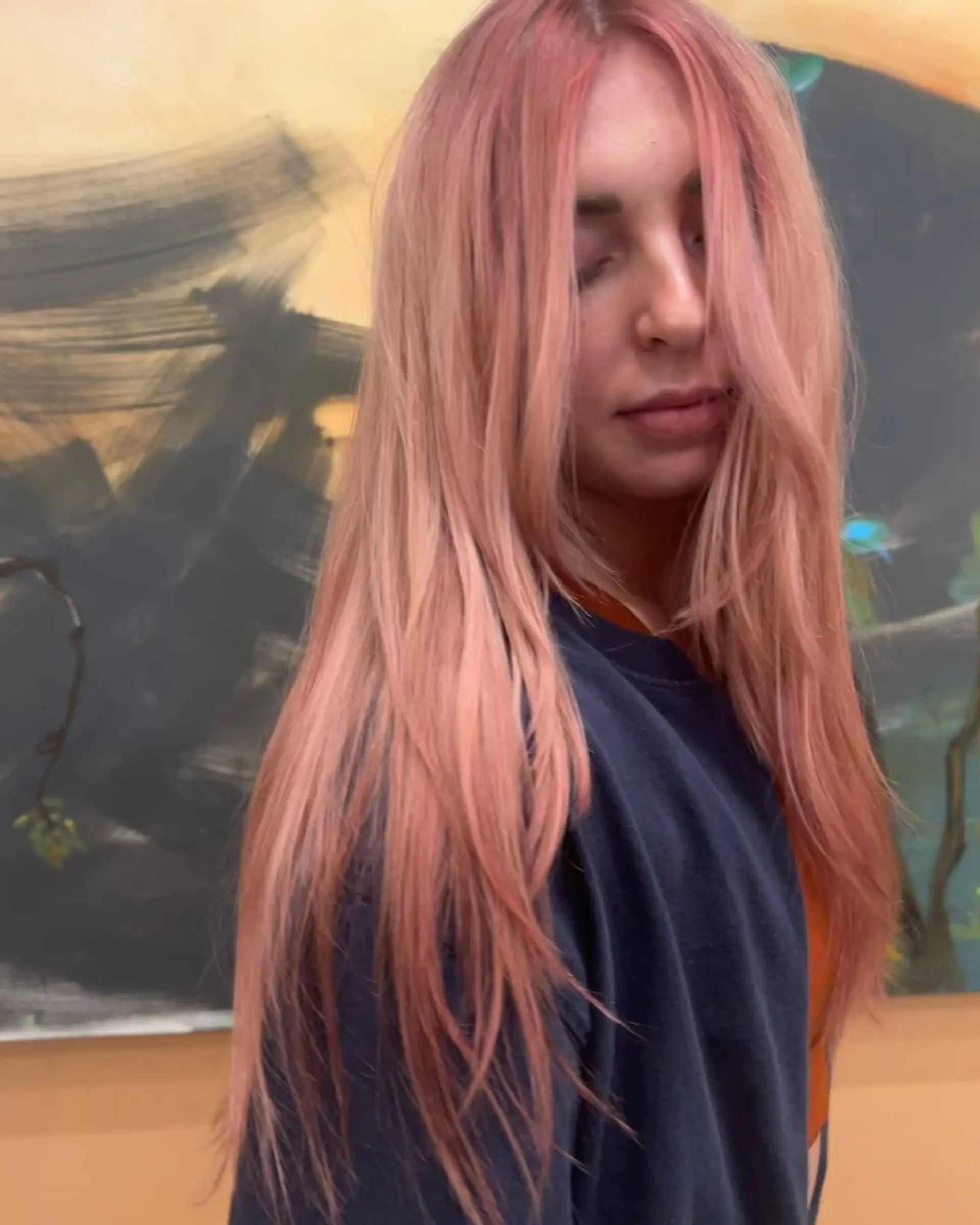 Long layered hair styled straight with face-framing pieces and colored in soft pastel rose gold. 1
