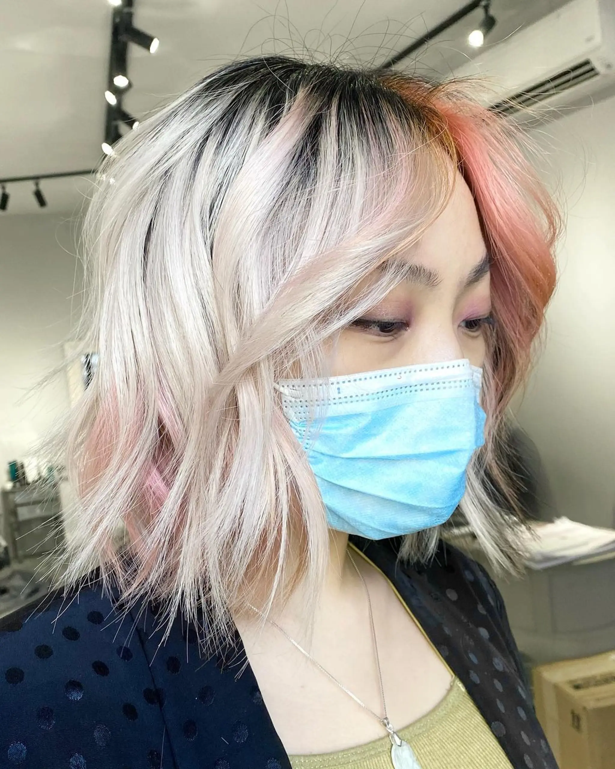 A chic, ombre medium-length bob with dark roots, transitioning to platinum blonde and pastel pink tips. Styled with gentle waves, a side part, and layered for texture and volume.
