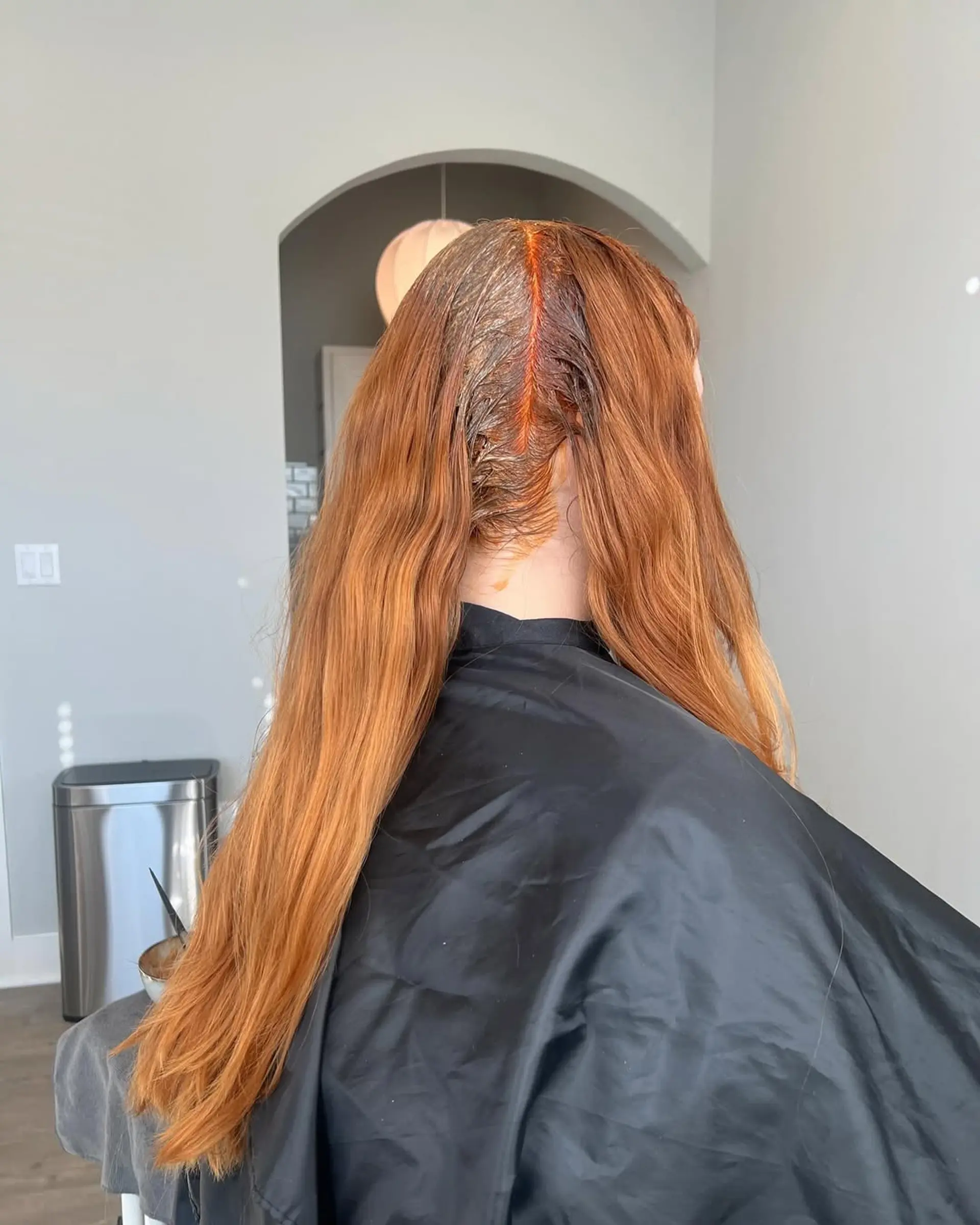 Long, wavy hair in a vibrant copper red shade, with a root color application in progress along the part. 1