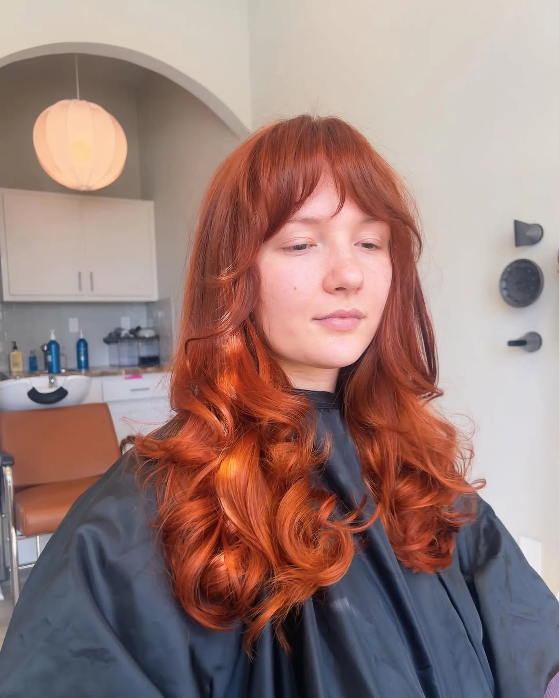 Long, wavy hair in a vibrant copper red shade, with a root color application in progress along the part. 2