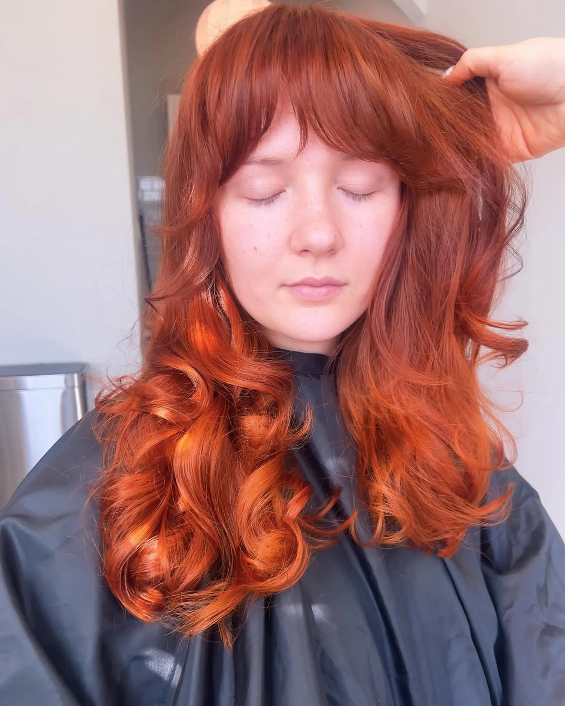Long, wavy hair in a vibrant copper red shade, with a root color application in progress along the part. 3