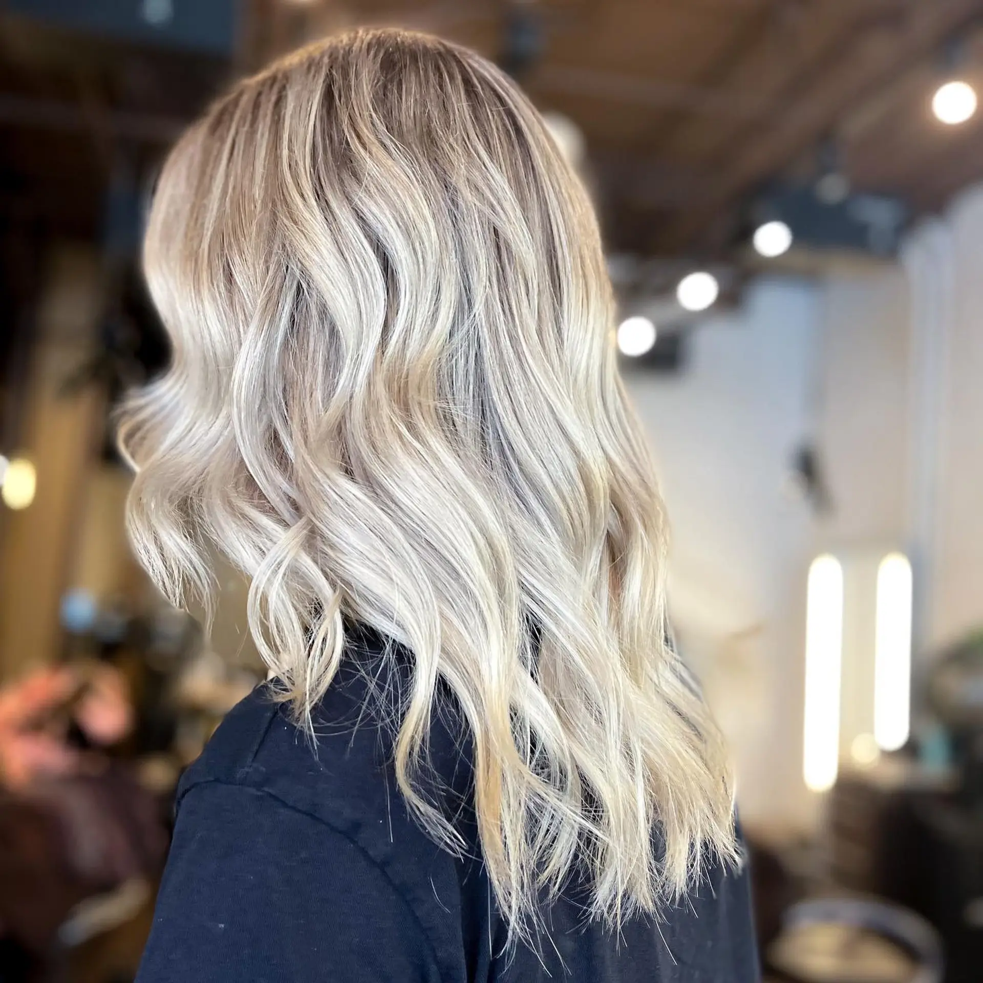 Medium-length wavy hair with an icy blonde balayage and rooted blonde look. 1