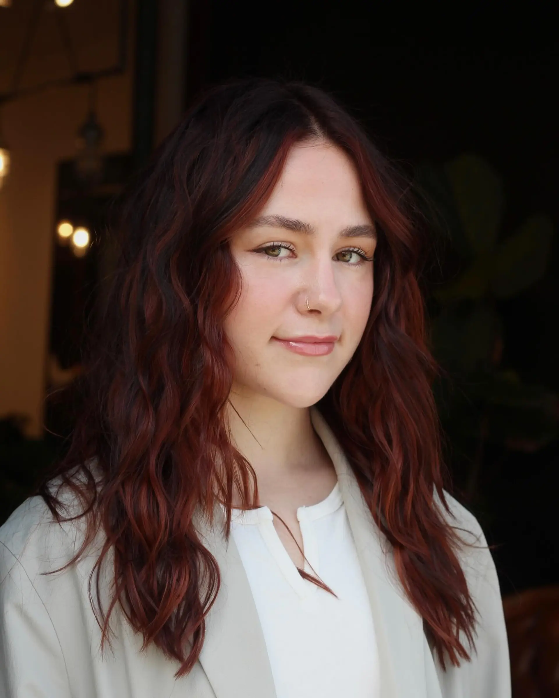Long layered hair styled in relaxed waves, featuring a dimensional soft copper balayage over a deep base with a center part. 1