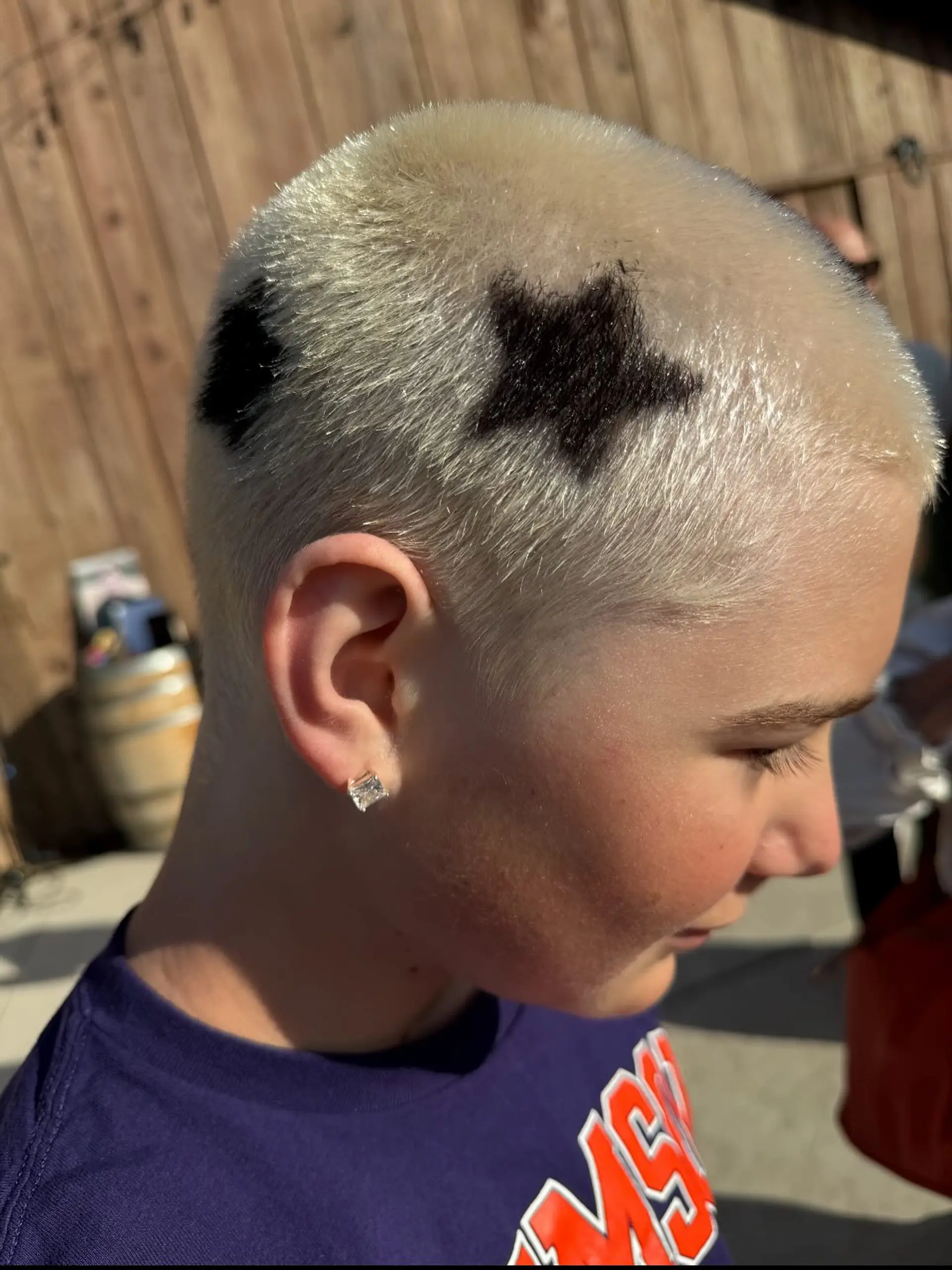 A platinum blonde buzz cut featuring stenciled or painted black star designs on the side. 1