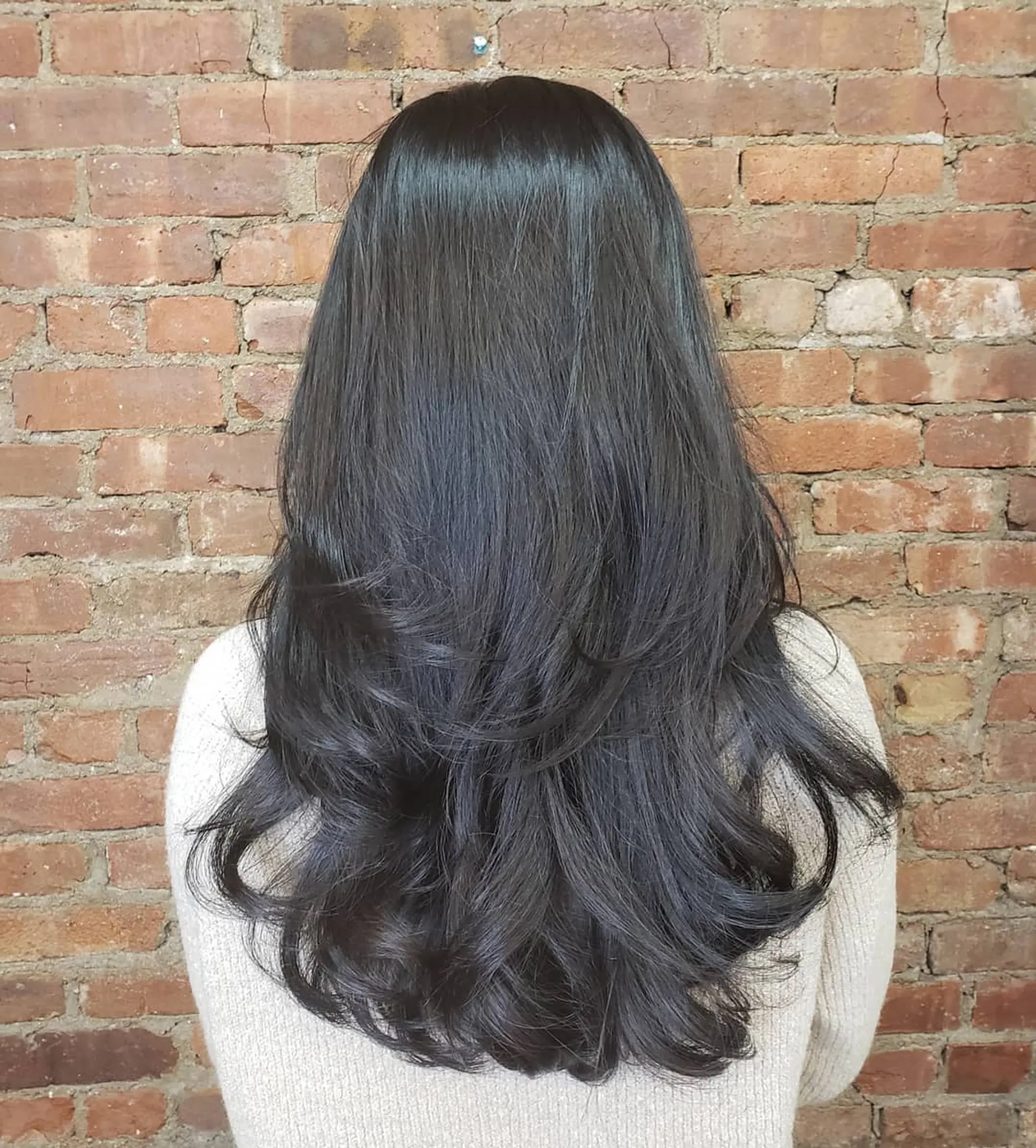 Long dark hair cut in flowing layers with soft, rounded flipped-in ends and a smooth, glossy finish. 1