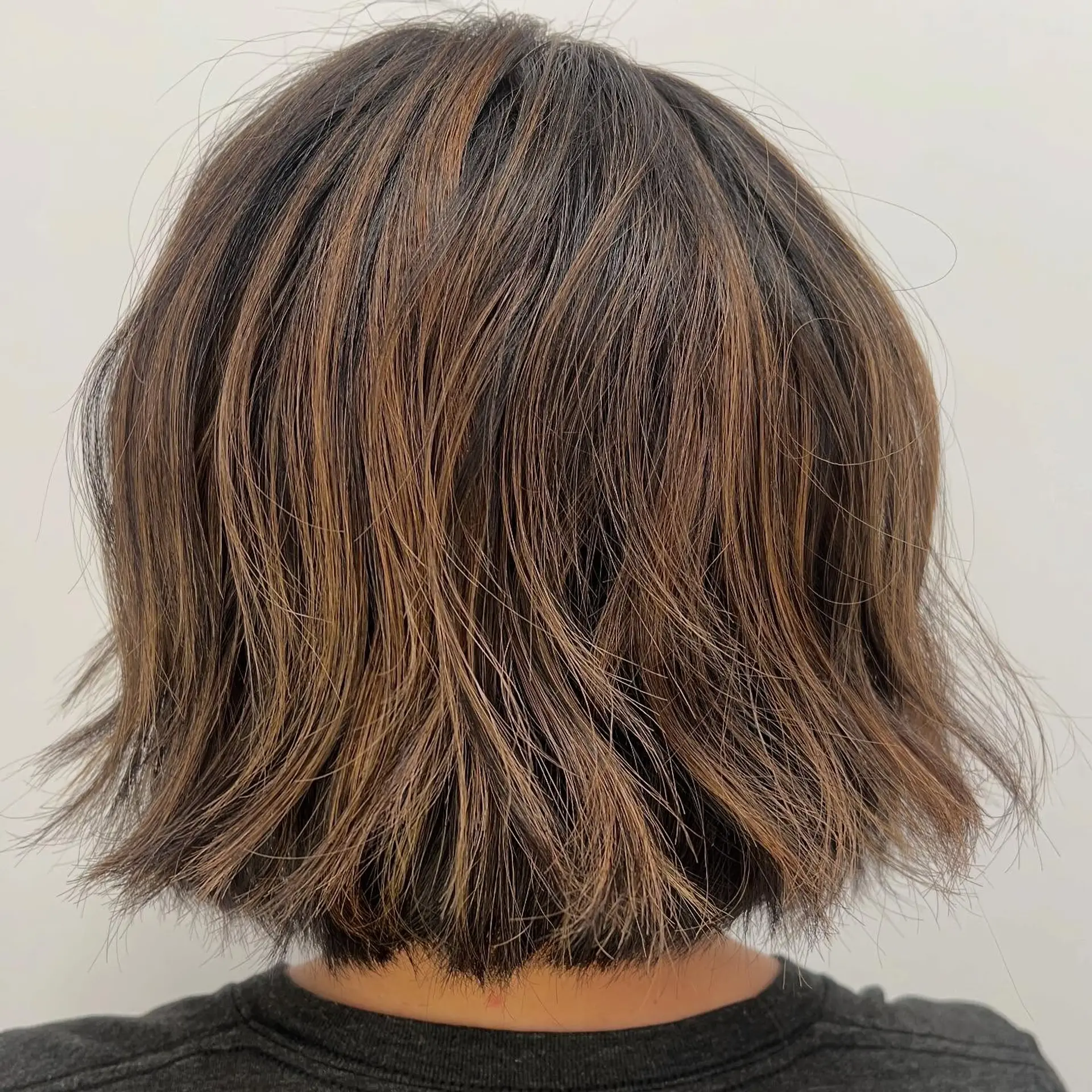 A neck-length textured short bob featuring subtle caramel highlights and soft, piecey layers. 1