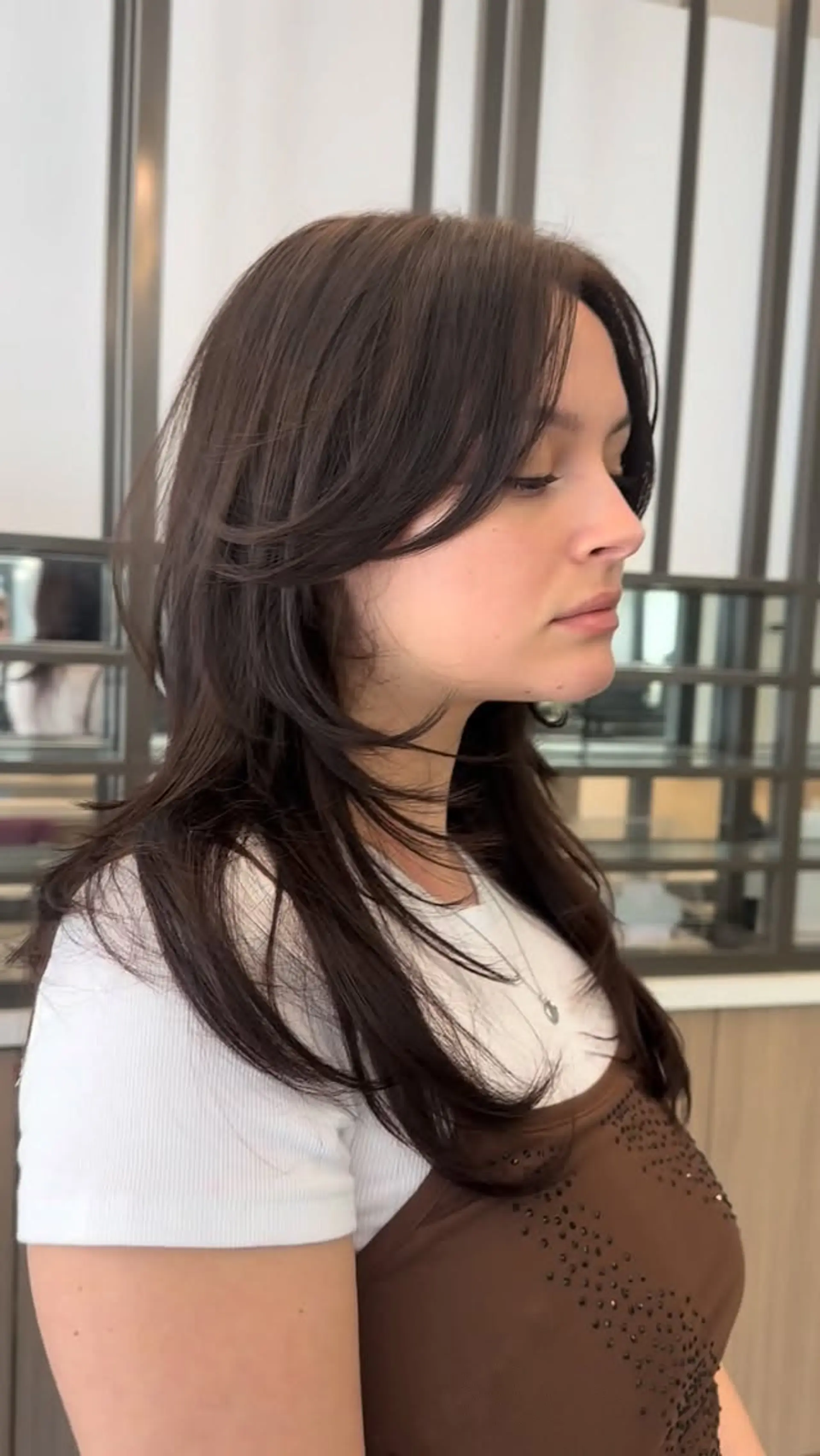 A medium-length hush cut with soft, feathery layers and face-framing curtain bangs in a cool brown shade. 1