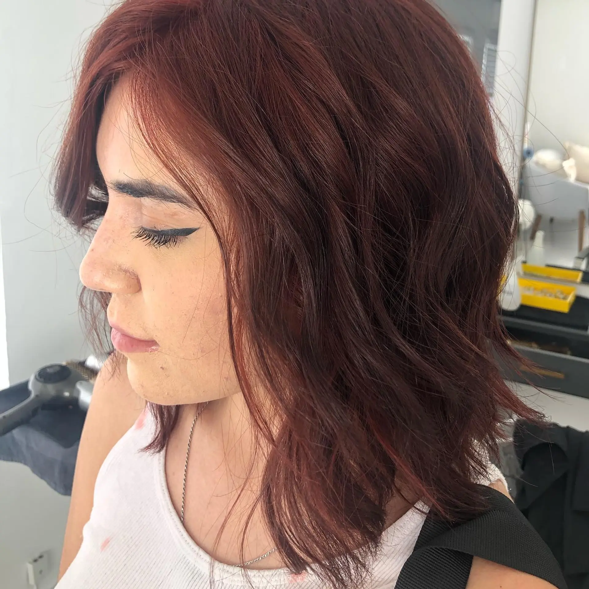 A textured shoulder-length lob styled with loose, relaxed waves in a deep red-brown shade. 1