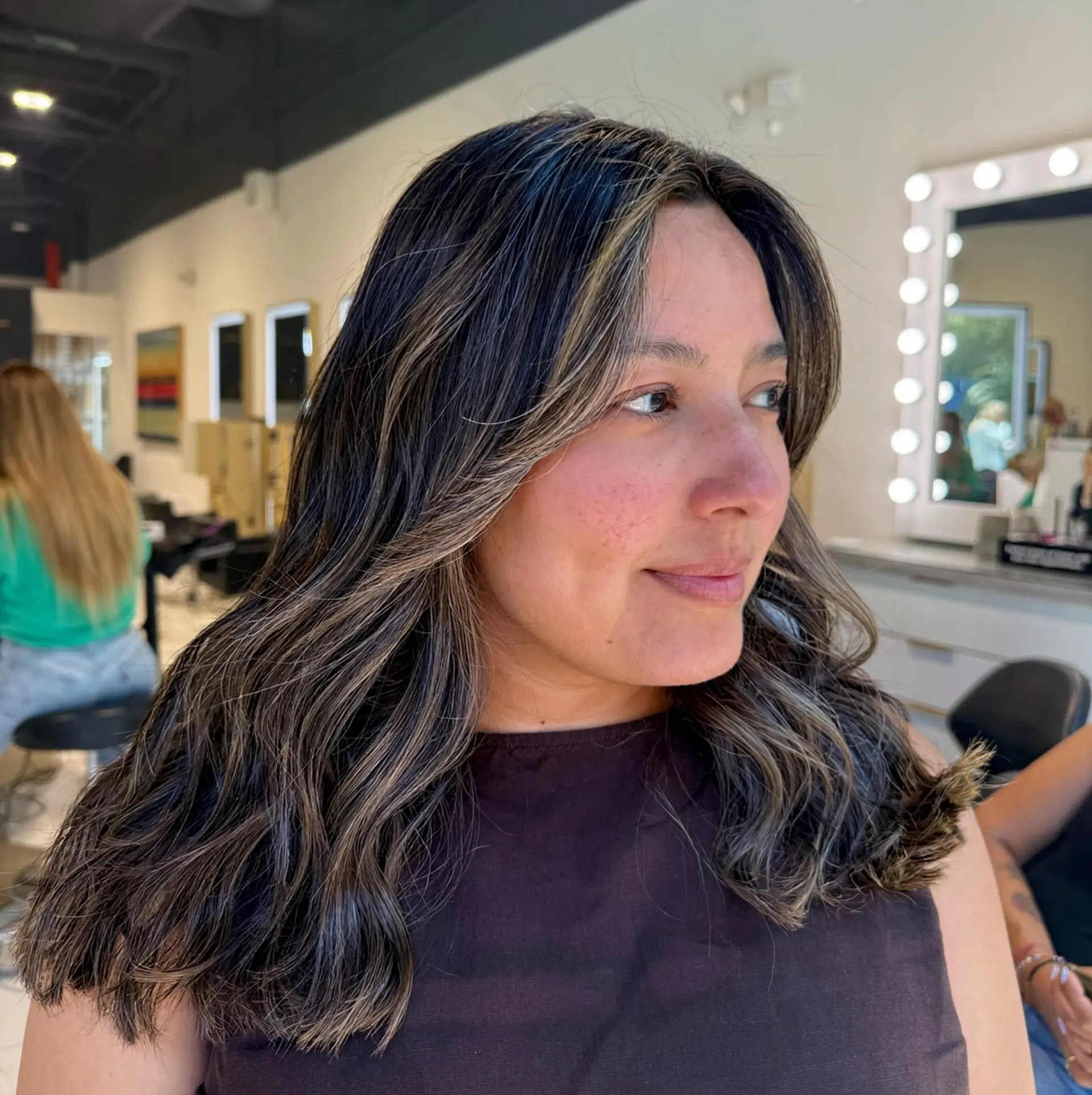 Medium-length wavy dark hair with subtle ash blonde babylights and balayage designed for seamless gray blending. 1