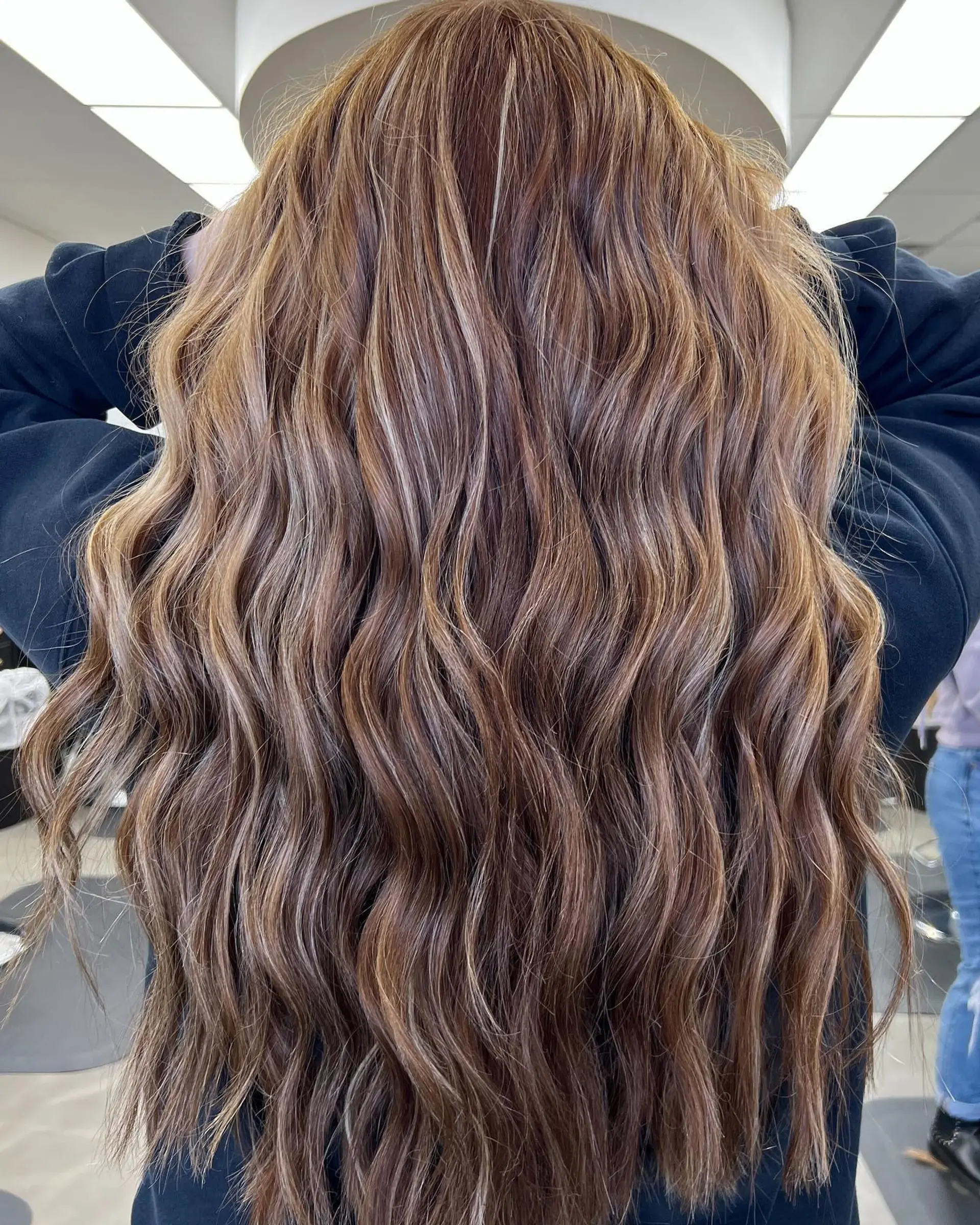 Long, dimensional brunette hair colored with warm caramel accents and styled in soft, cascading waves. 1