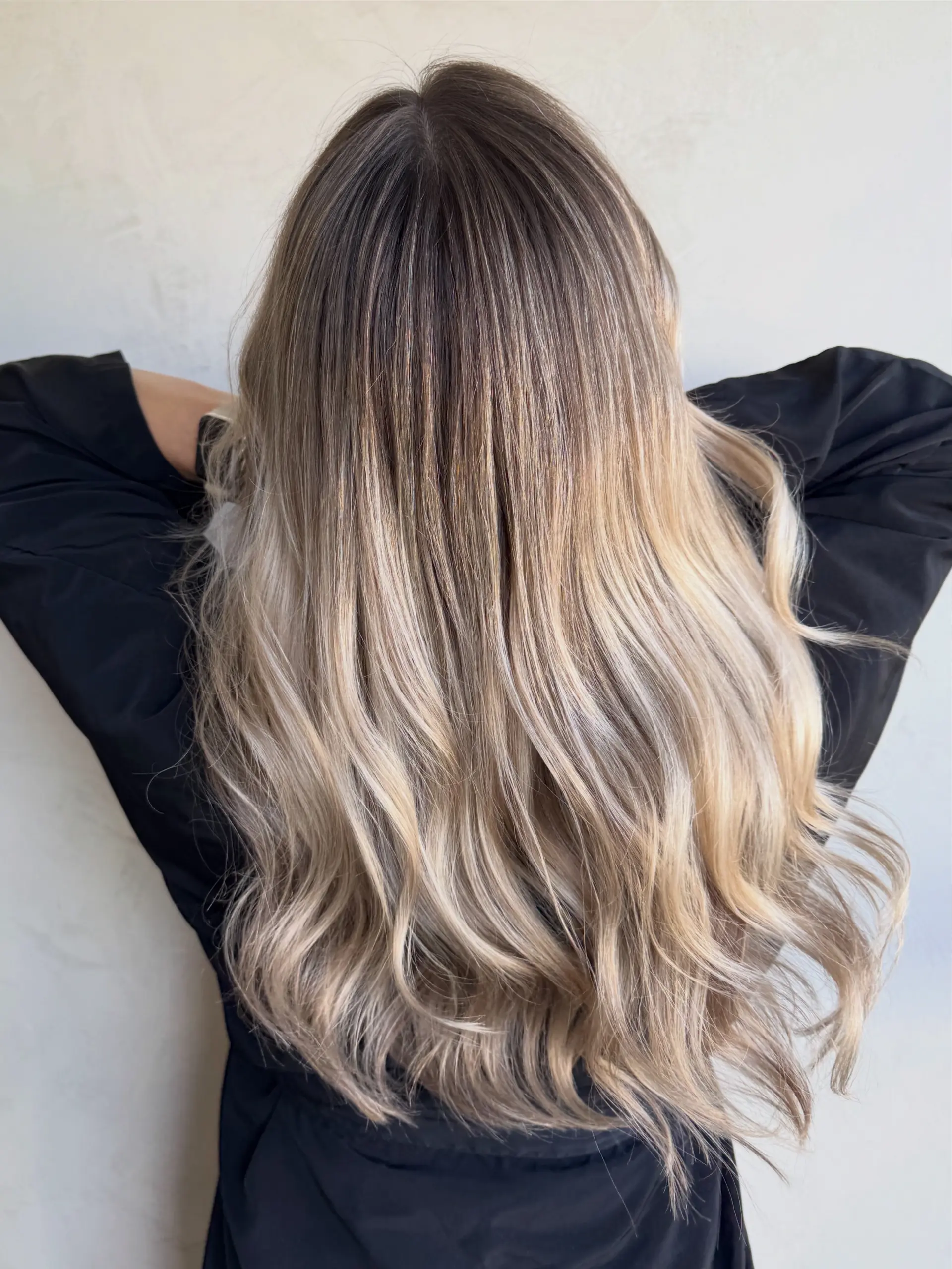 Long dimensional blonde hair featuring a seamless root shadow transitioning into bright cool blonde ribbons with soft, undone waves. 1