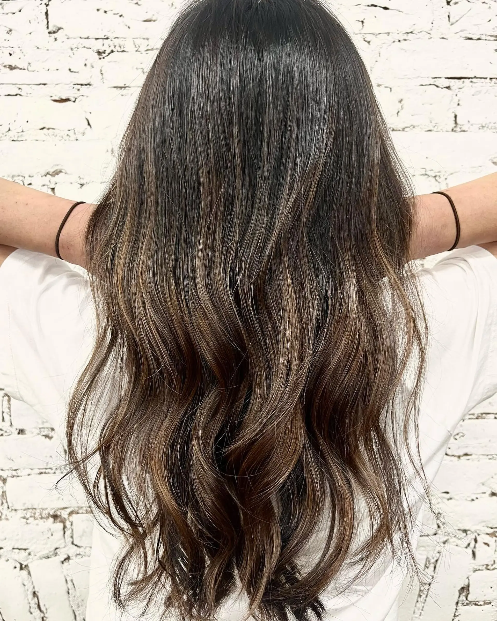 Long dark brunette hair enhanced with fine dimensional highlights and styled into soft, textured waves. 1