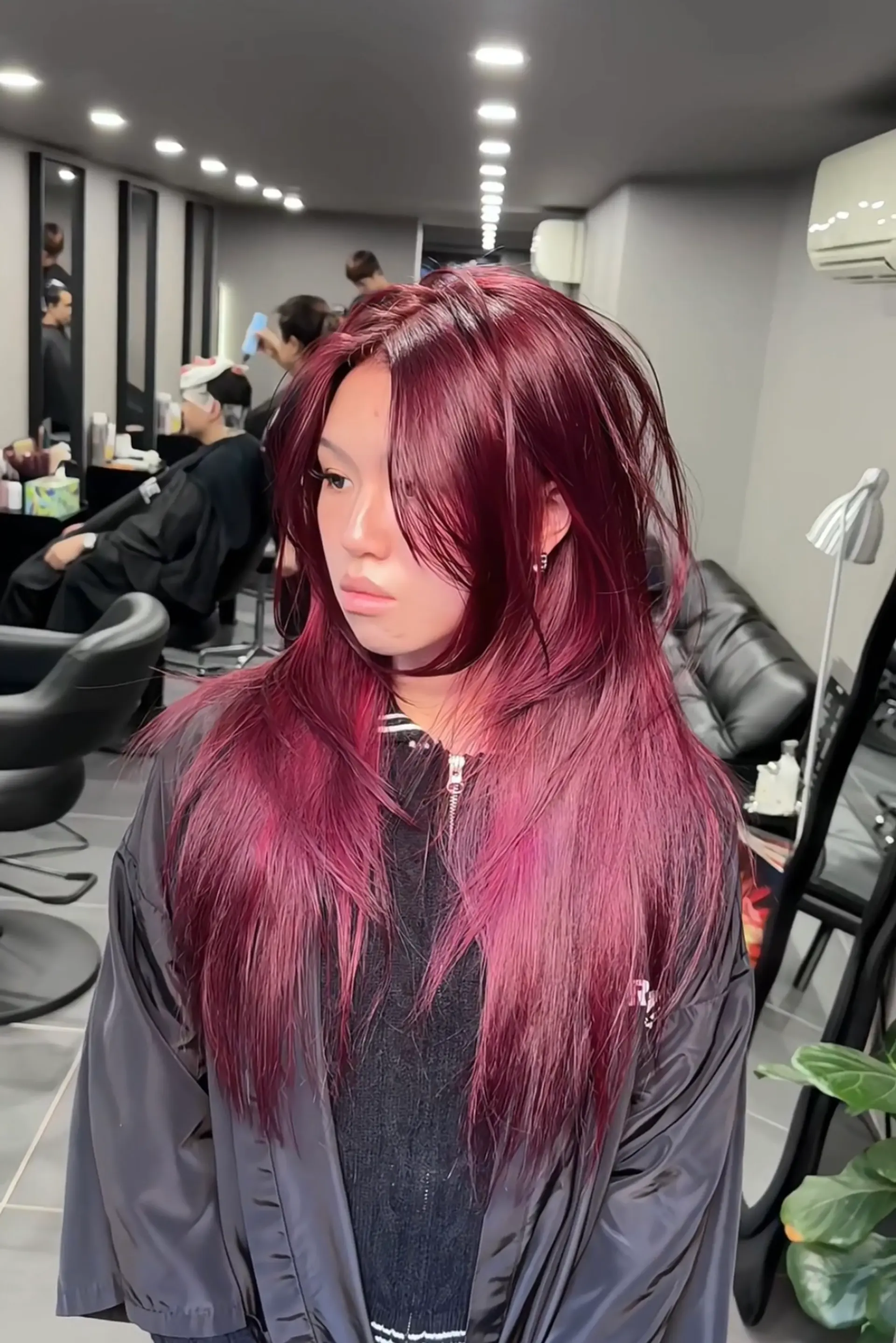 The hairstyle is a long, layered look with straight texture and a vibrant burgundy hue. It features voluminous layers and side-swept bangs, creating a dynamic and textured appearance. 4