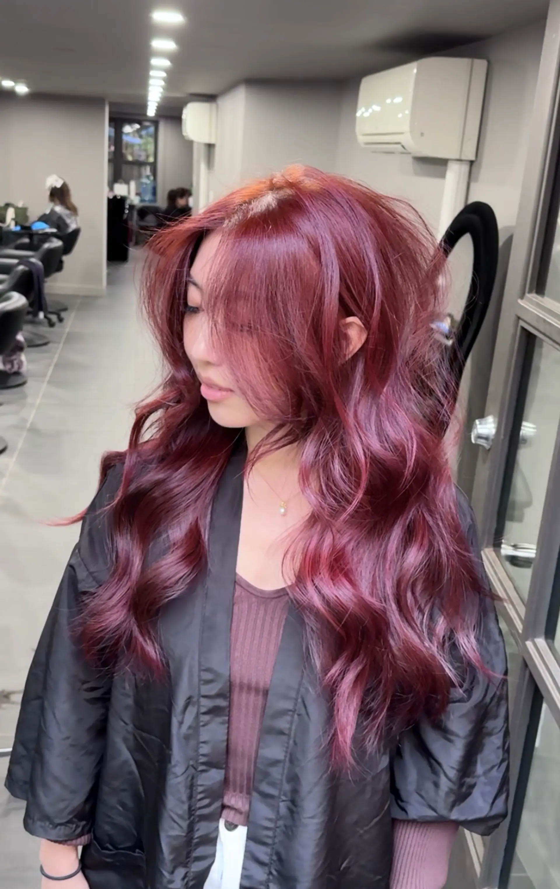 The hairstyle is a long, layered look with straight texture and a vibrant burgundy hue. It features voluminous layers and side-swept bangs, creating a dynamic and textured appearance. 5