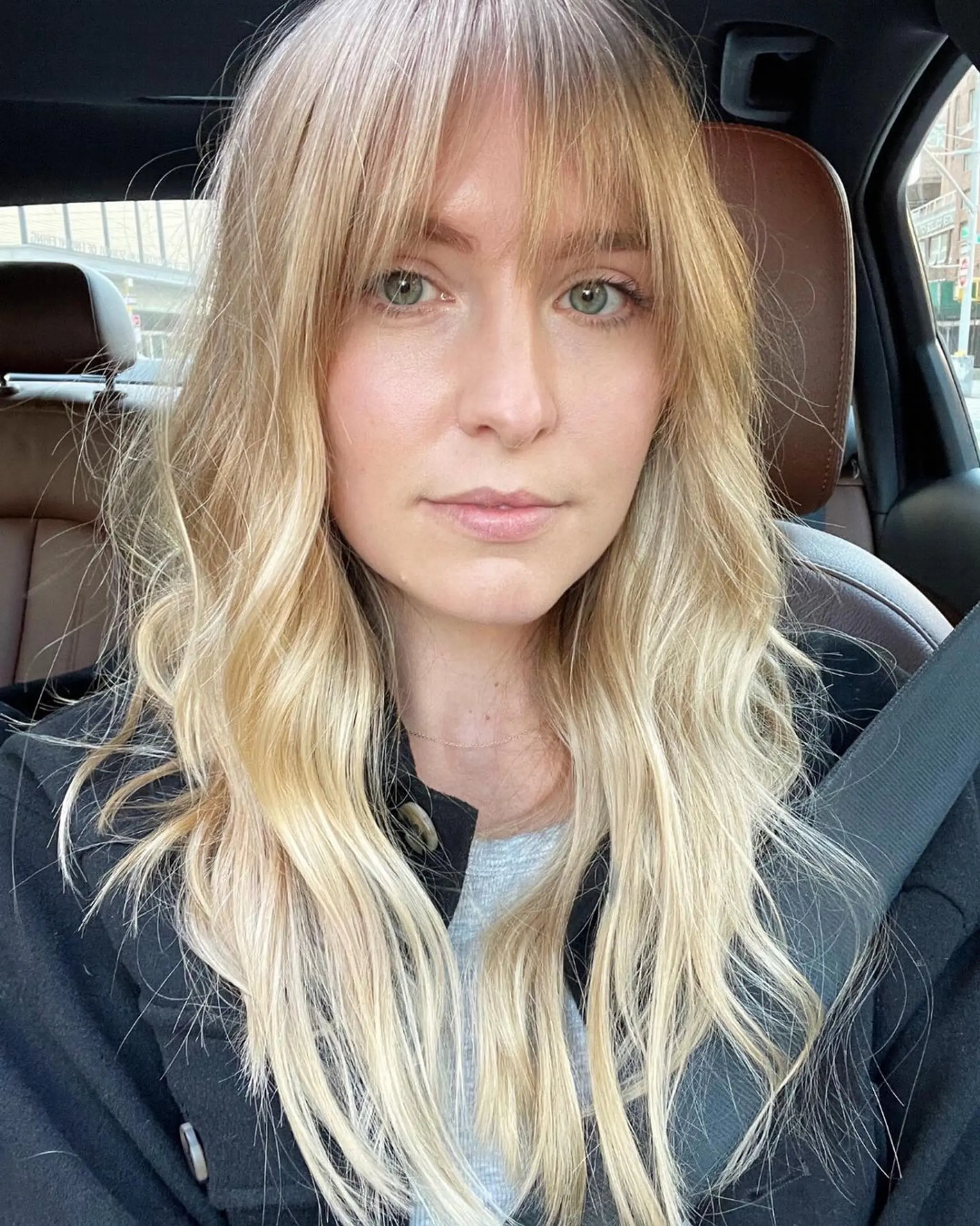 A long, wavy blonde hairstyle with a full fringe, featuring loose waves, layered ends, and a sun-kissed color with light brown undertones.